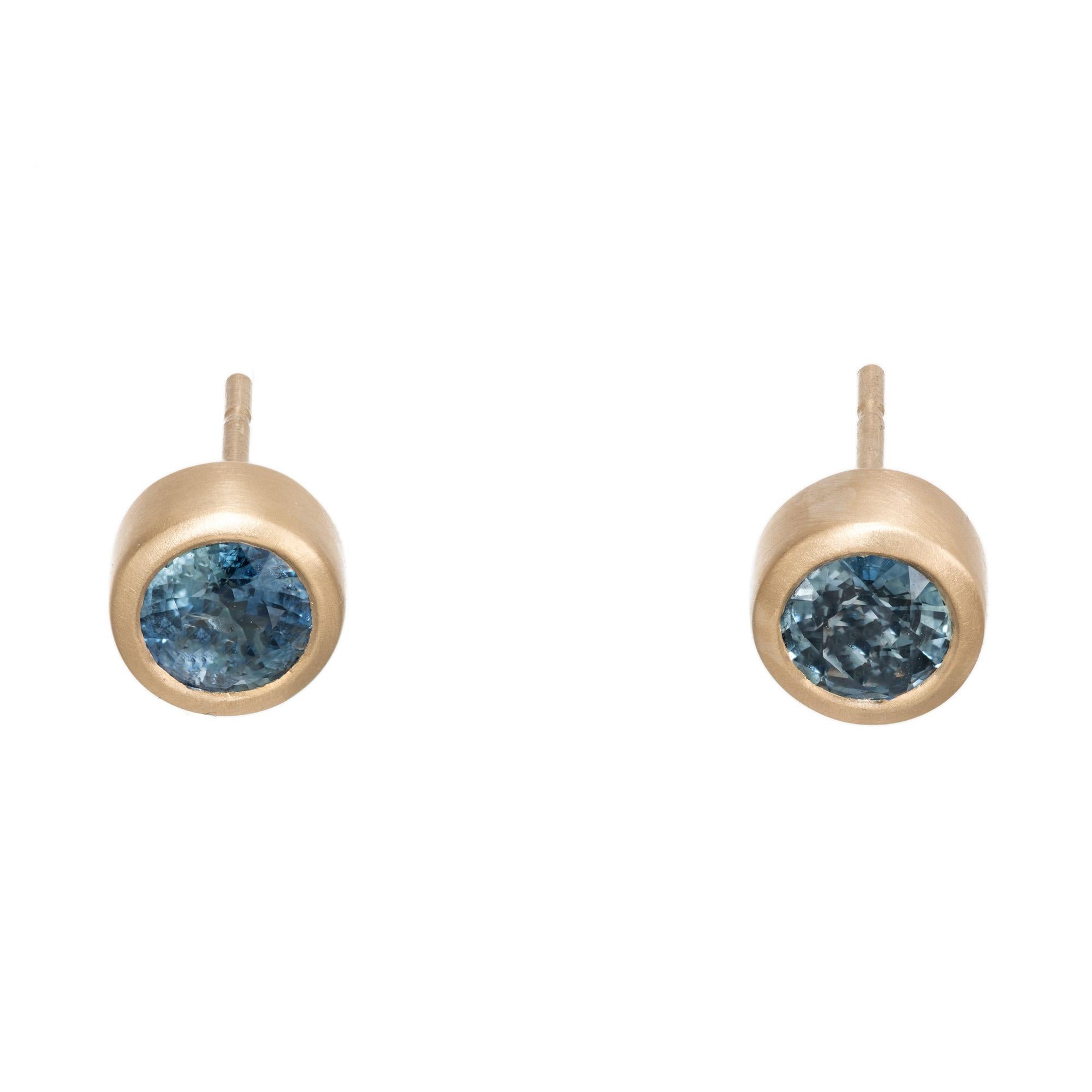 Blue slightly greenish sapphire bezel set sapphire stud earrings. 2 round cut Ceylon sapphires with an approximate carat total weight of .98cts, set in soft brush nickel 18k yellow gold tube bezel settings. These sapphire have unique coloring, blue