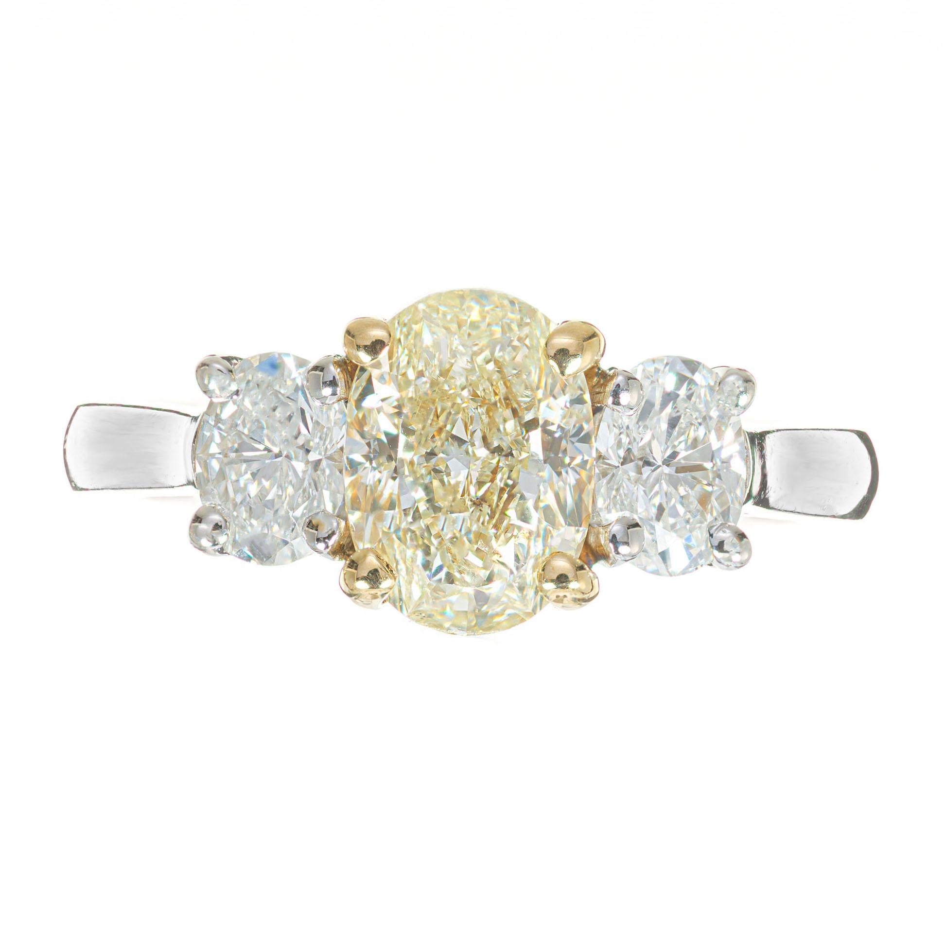 Three-stone oval yellow diamond 18k white gold engagement ring. This handmade setting from the Peter Suchy Workshop is set with a EGL certified fancy light yellow oval center diamond, accented with 2 oval white diamonds, in a three-stone 18k white