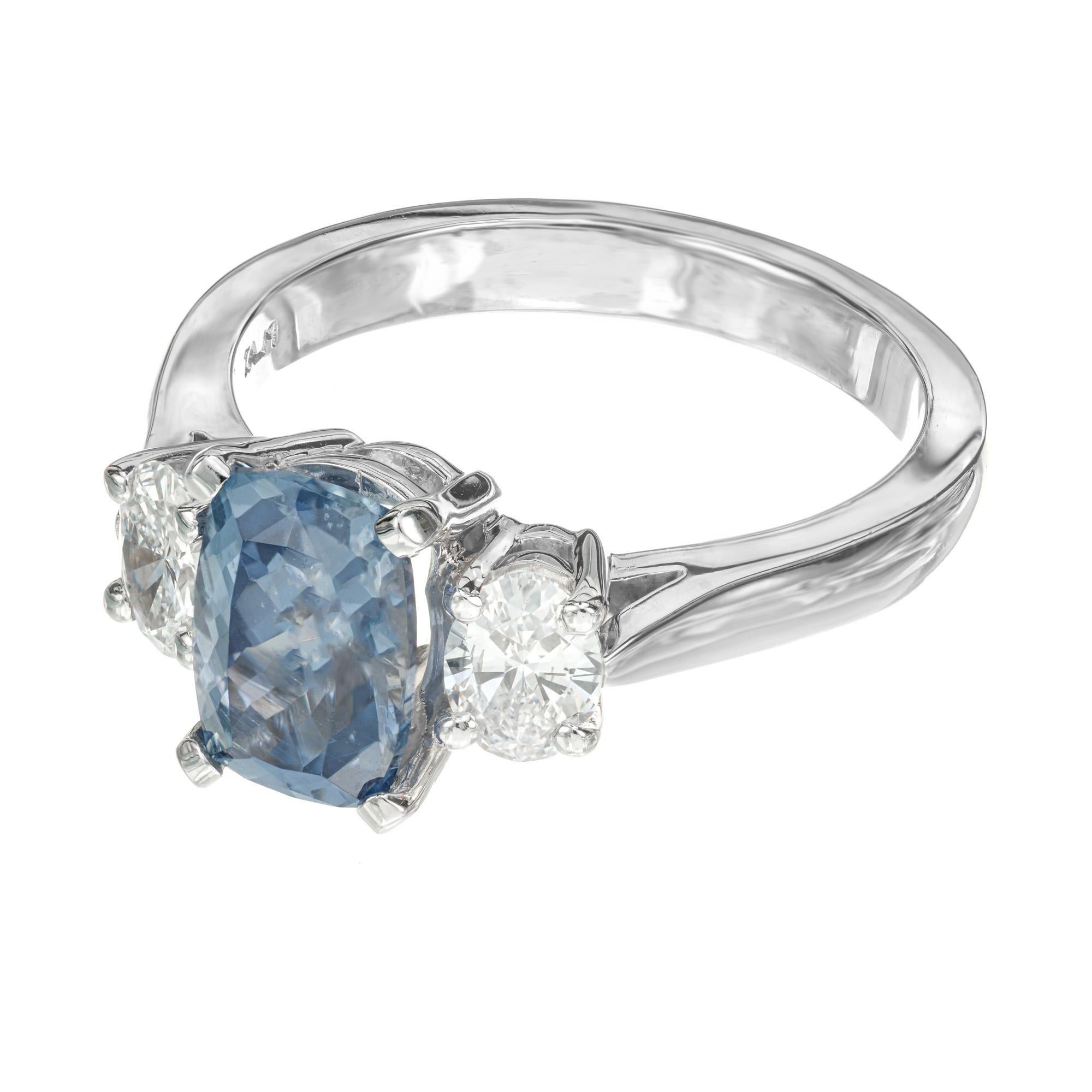 The centerpiece of this engagement ring is an oval natural grayish blue 2.23ct sapphire, which is certified by the GIA as natural, no heat. The sapphire is mounted in a platinum three-stone setting with one oval sparkling diamond on each side of the