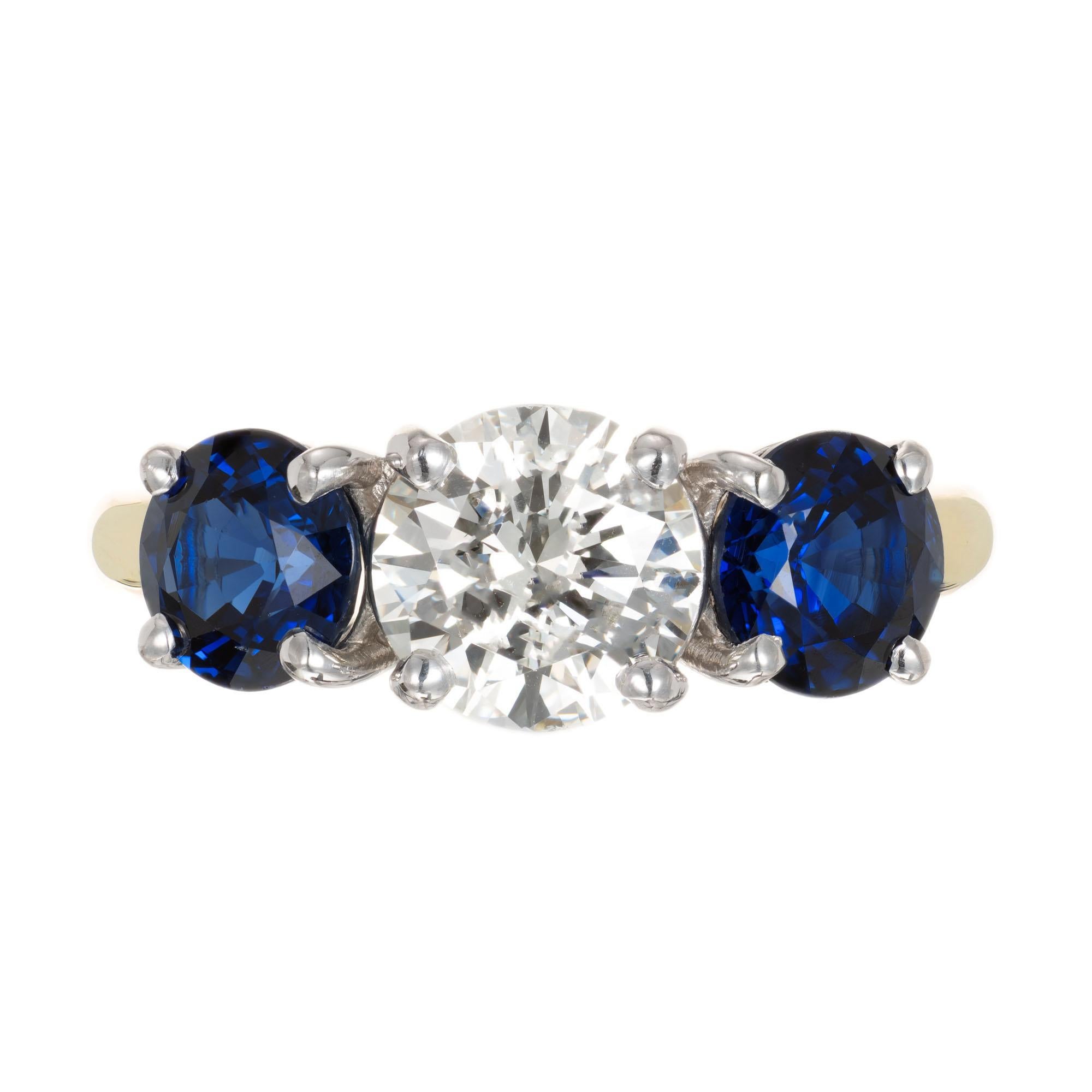 Peter Suchy three-stone diamond and sapphire engagement ring. Platinum and 14k yellow gold setting with a GIA certified round brilliant cut center stone, accented with 2 round sapphires. 

1 round brilliant cut diamond, K VS2 approx. 1.22cts GIA