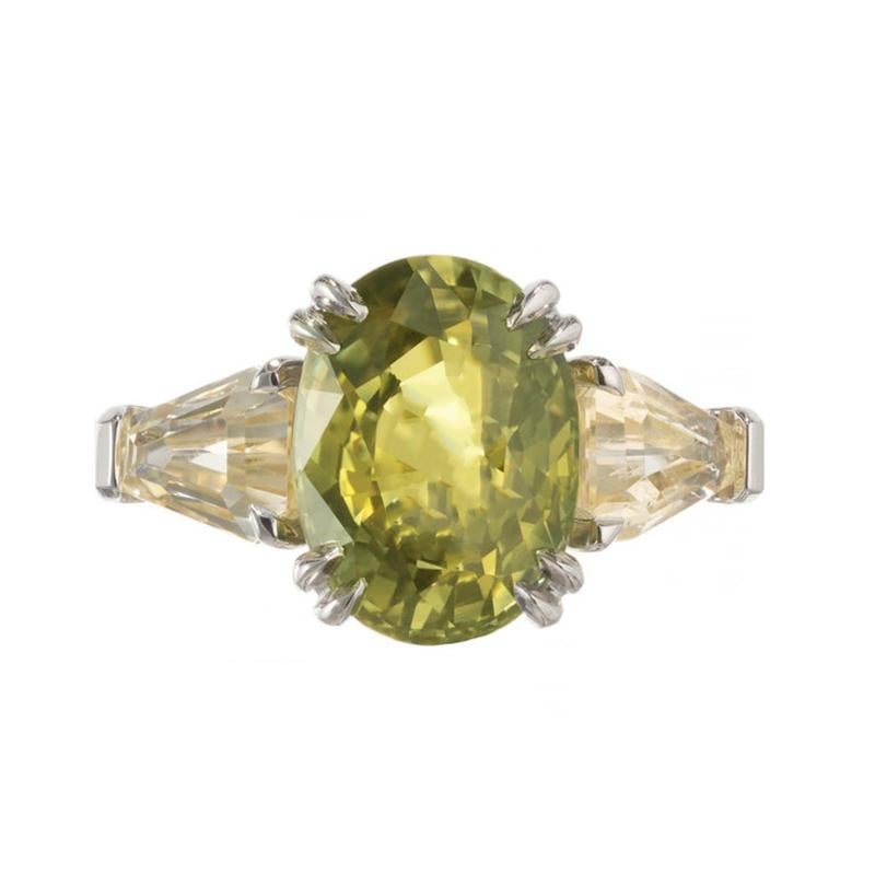 Exceptional green and yellow oval Sapphire and diamond three-stone engagement ring. Simply put, this ring is spectacular. GIA certified oval yellow and green center sapphire mounted in a platinum setting that is accented by two shield step cut