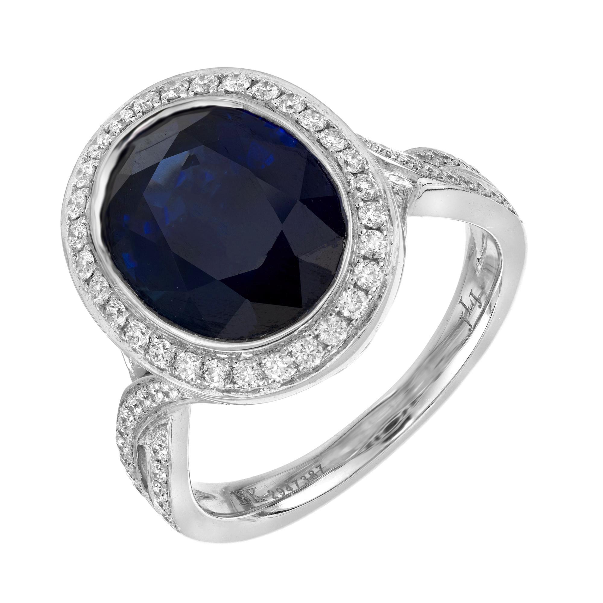Stunning deep blue natural oval sapphire and diamond engagement ring. At the center of this setting is a rich deep blue oval sapphire mounted and bezel set in 18k white gold. The sapphire is accented by a halo of round brilliant cut diamonds. The