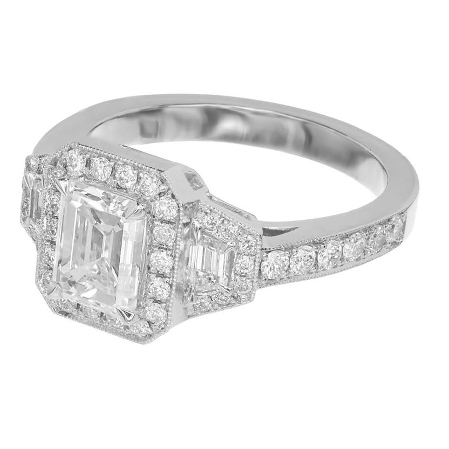Emerald step cut center diamond engagement ring. GIA certified Emerald step cut 1.11ct center stone with a halo of round diamonds accented with 2 trapezoid Deco step cut side diamonds each with a halo of round cut diamonds in a platinum setting with