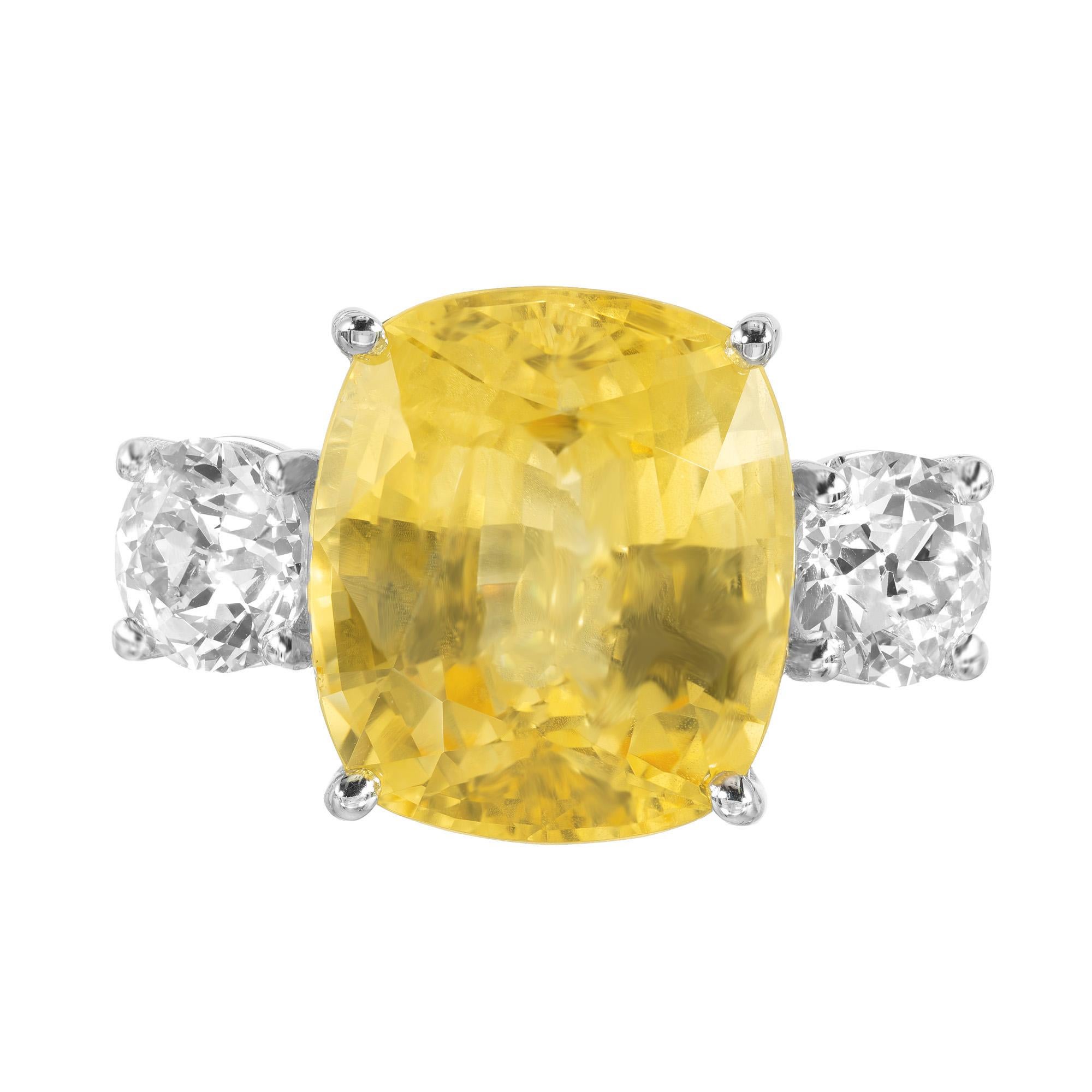 Superbe bague de fiançailles à trois pierres en saphir jaune et Dimaond. Au cœur de cette bague se trouve un saphir jaune spectaculaire de 13,70ct, de taille coussin, naturel et non chauffé. La pierre précieuse est rehaussée de deux diamants