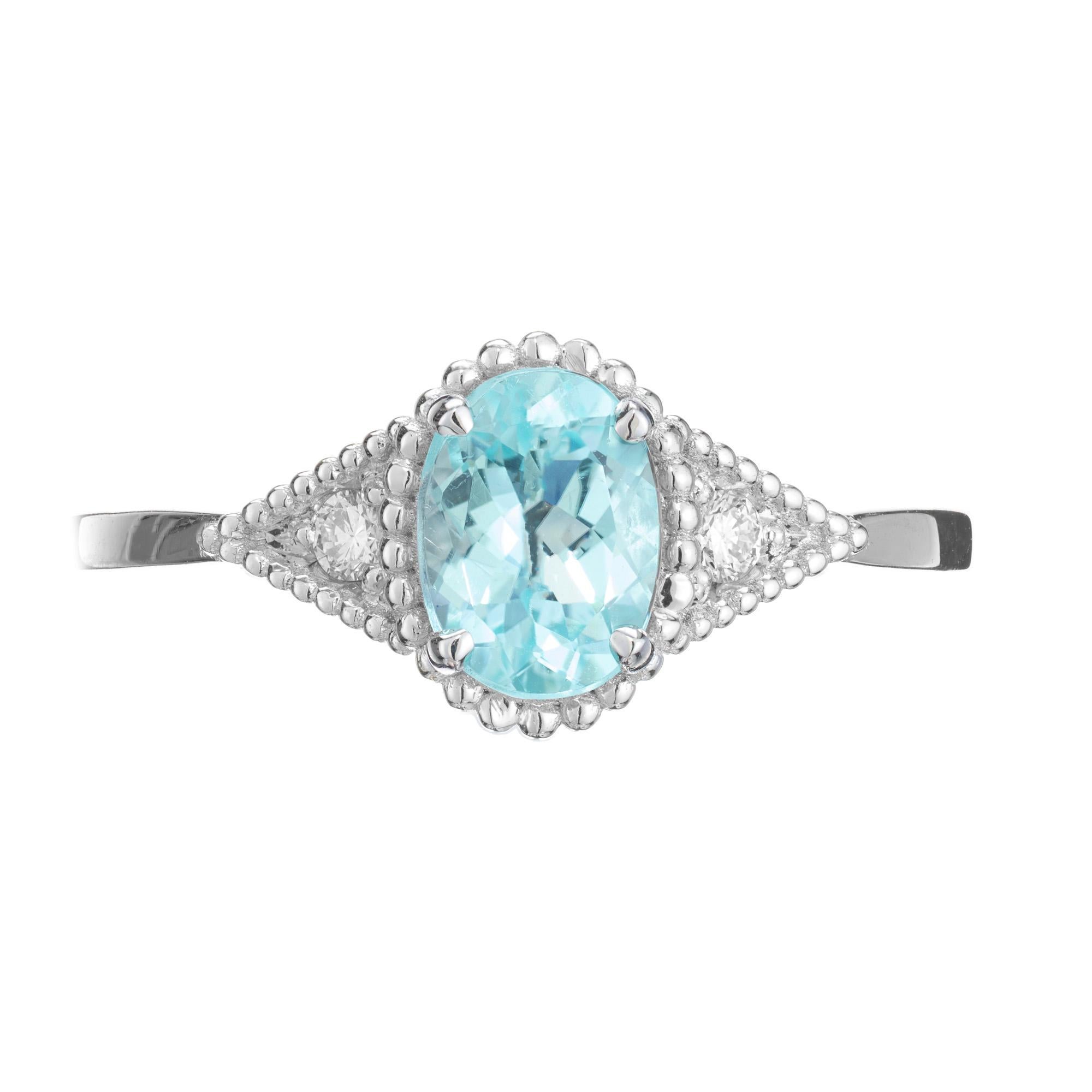 Tourmaline and diamond engagement ring. GIA Certified .71cts neon blue oval tourmaline mounted in a four prong 18k white gold setting with two round cut accent diamonds on each side. Bead halos frame the diamond and tourmaline. GIA has certified