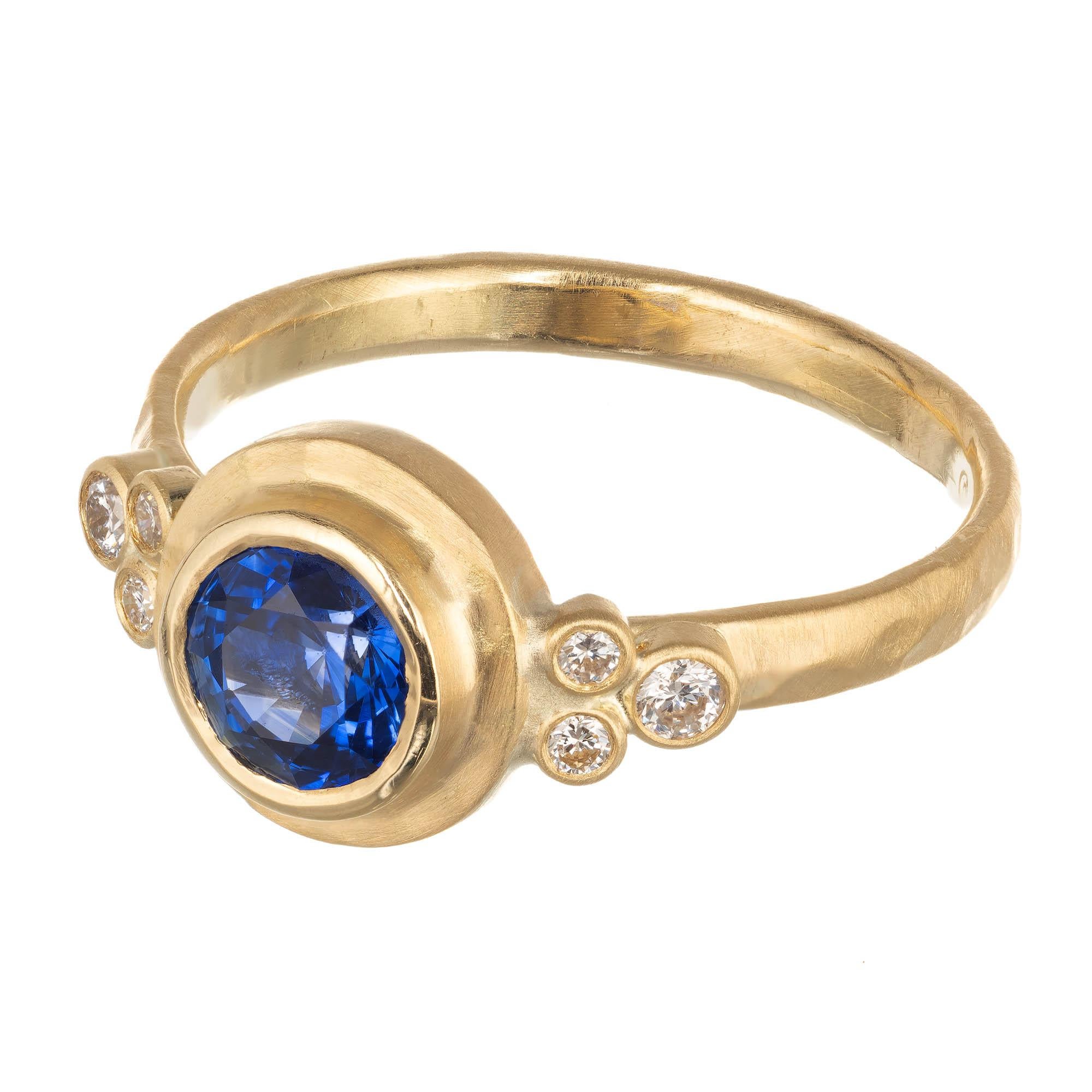 Peter Suchy sapphire and diamond hammered engagement ring. Center sapphire is bezel set with a hammered halo design. 3 diamonds set on the each side of the 18k yellow gold setting. The entire setting is hammered design in the Peter Suchy Workshop,