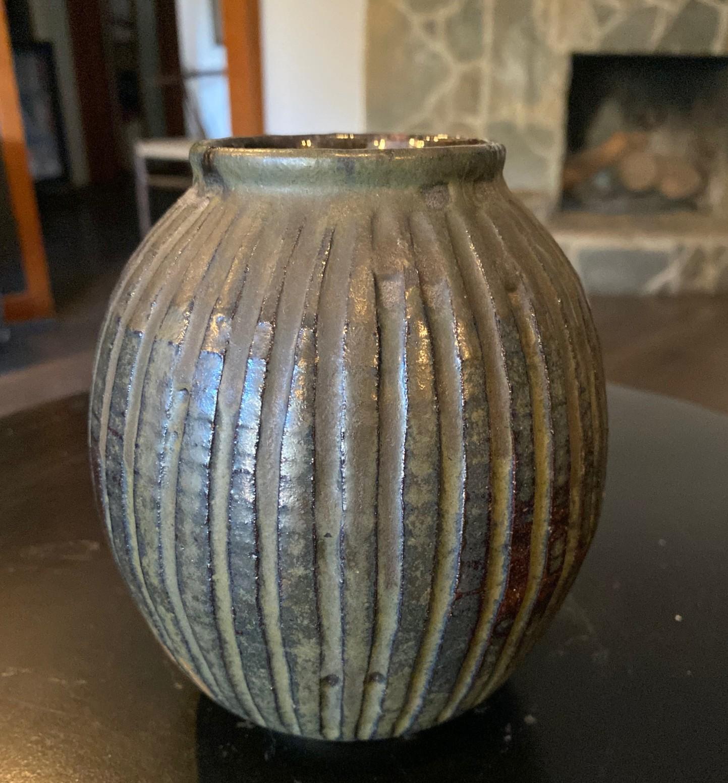 A fantastic early stoneware California studio pottery vase (circa early 1950s) by Master Greek-American potter/artist Peter Voulkos featuring a ribbed design and dark, luminous glaze that radiates in the light.  

Signed on base with incised