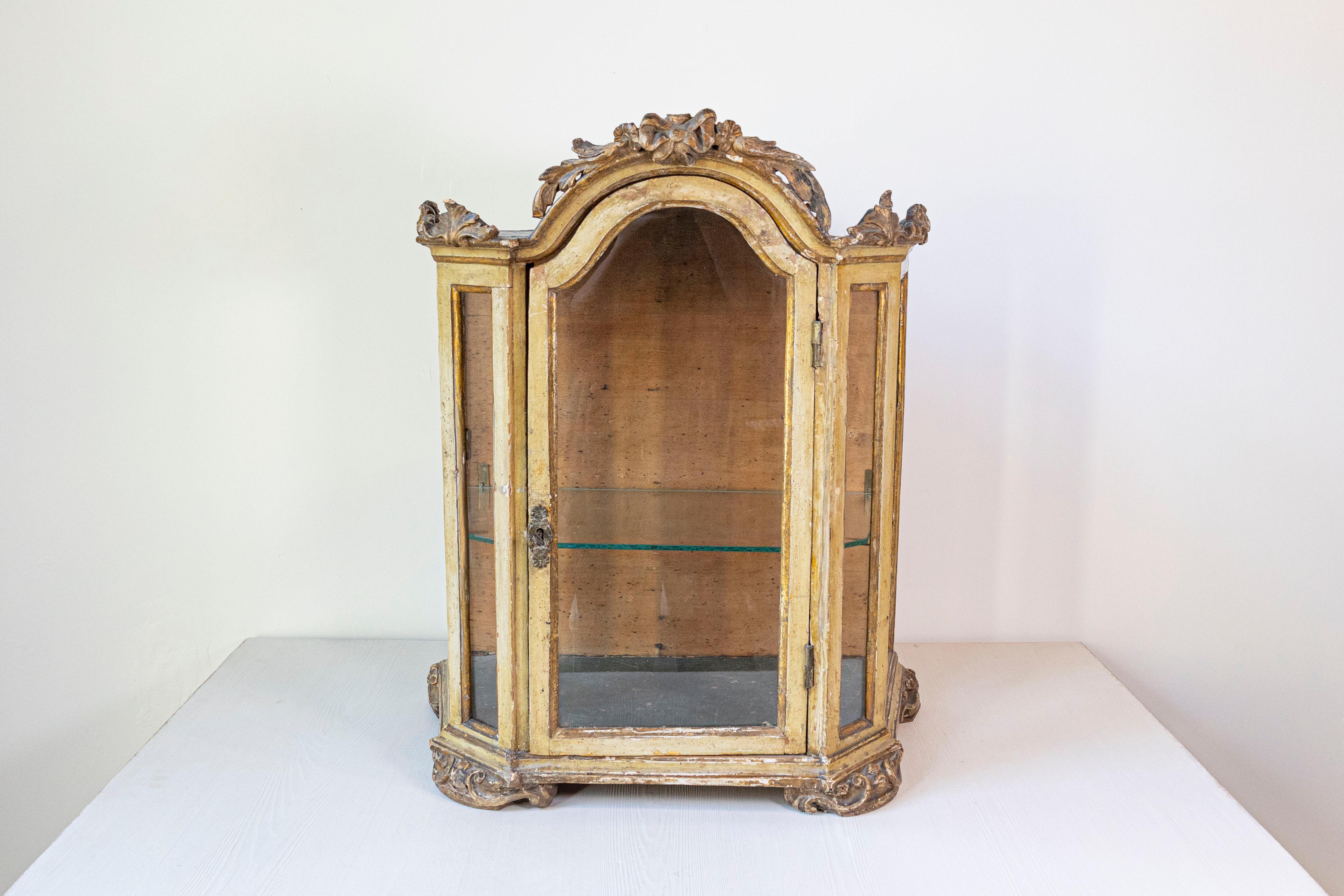 Piccola vetrina veneziana di epoca rococò del XVIII secolo in legno dipinto con stemma intagliato e porta in vetro. Creata in Italia durante il periodo rococò, questa vetrinetta da tavolo italiana presenta uno squisito stemma floreale intagliato a