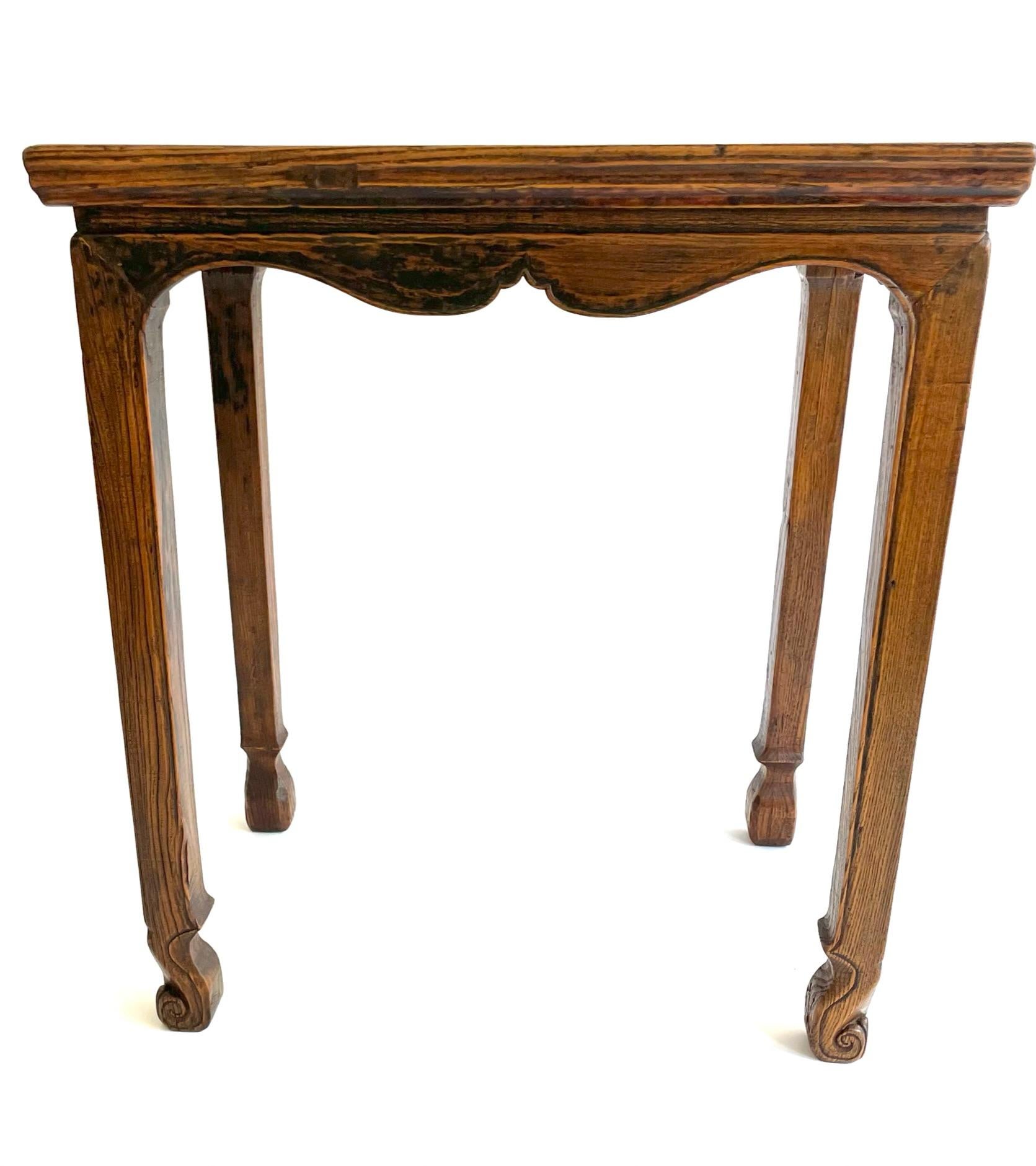 This unusual 19th century petite wine table is carved from Yumu (Chinese Northern Elm) and is from the Shanxi province of northern China. The table is made with traditional mortise and tenon construction. The legs are gracefully carved with a