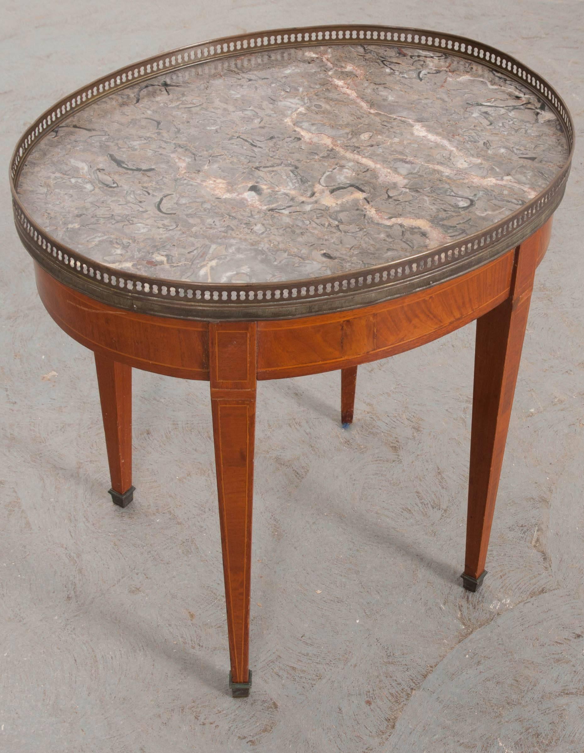 A lovely little mahogany table, oval in shape, from 19th century, France. The table has a gray marble top which is surrounded by a pierced brass gallery. It is made in the Directoire style, with straight, tapered legs that extend from the front of