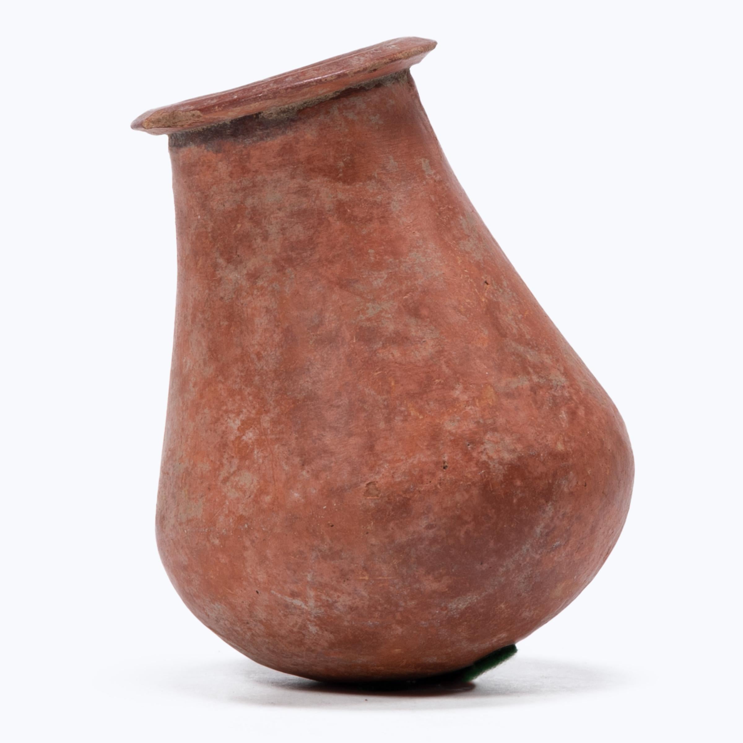 This petite hand-formed vessel bears a richly textured surface of worn red clay slip and dark smoke marks. Likely intended for everyday use, the simple bottle-form vessel reflects the skill of West African artisans, beautifully sculpted with