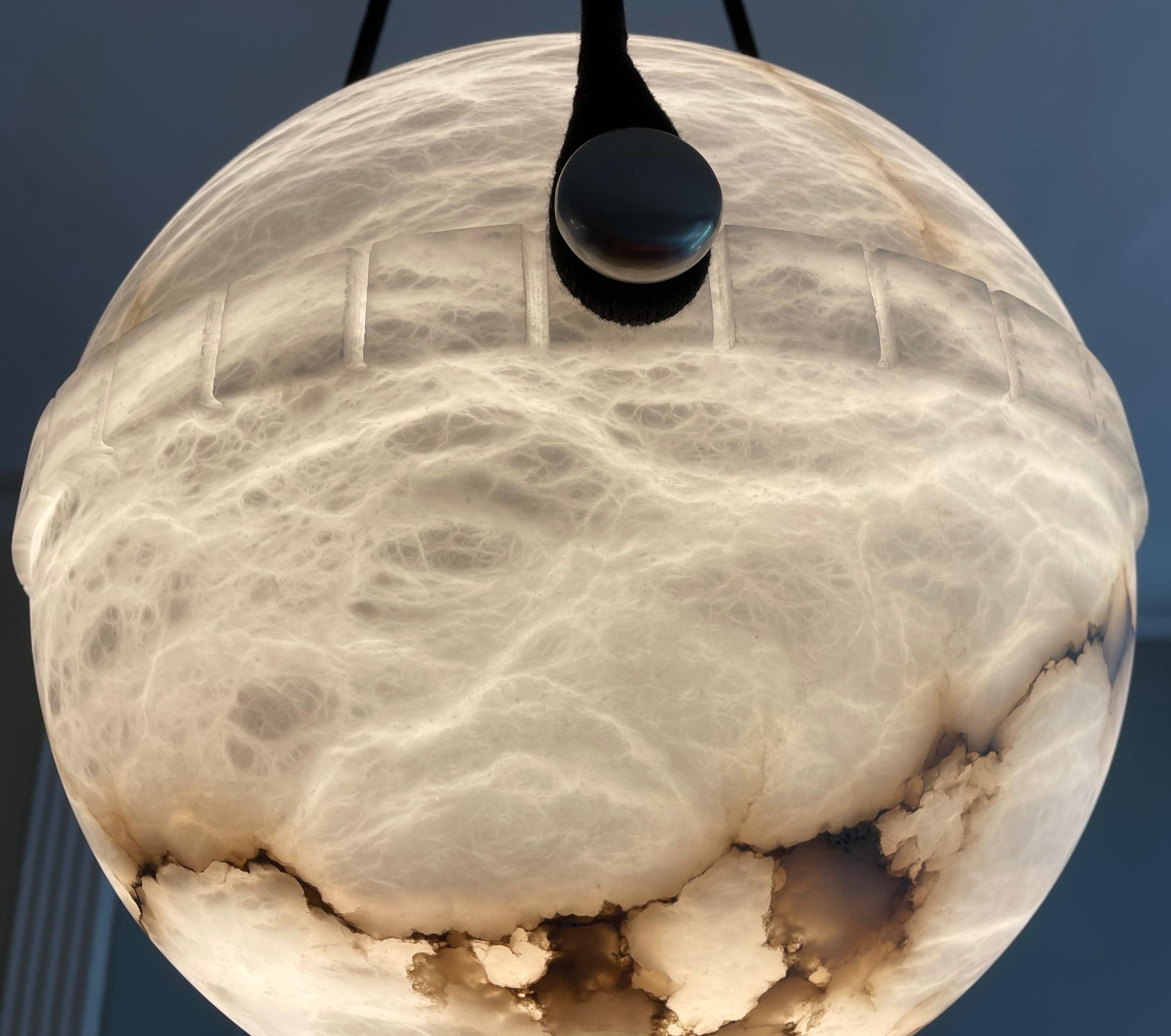 More unusual than the bowl shaped pendants, the globe alabaster features a lower half with a crisp dental motif on the central band and suspends on a set of three brushed nickel flattened balls. The upper half nestles perfectly into the banding and