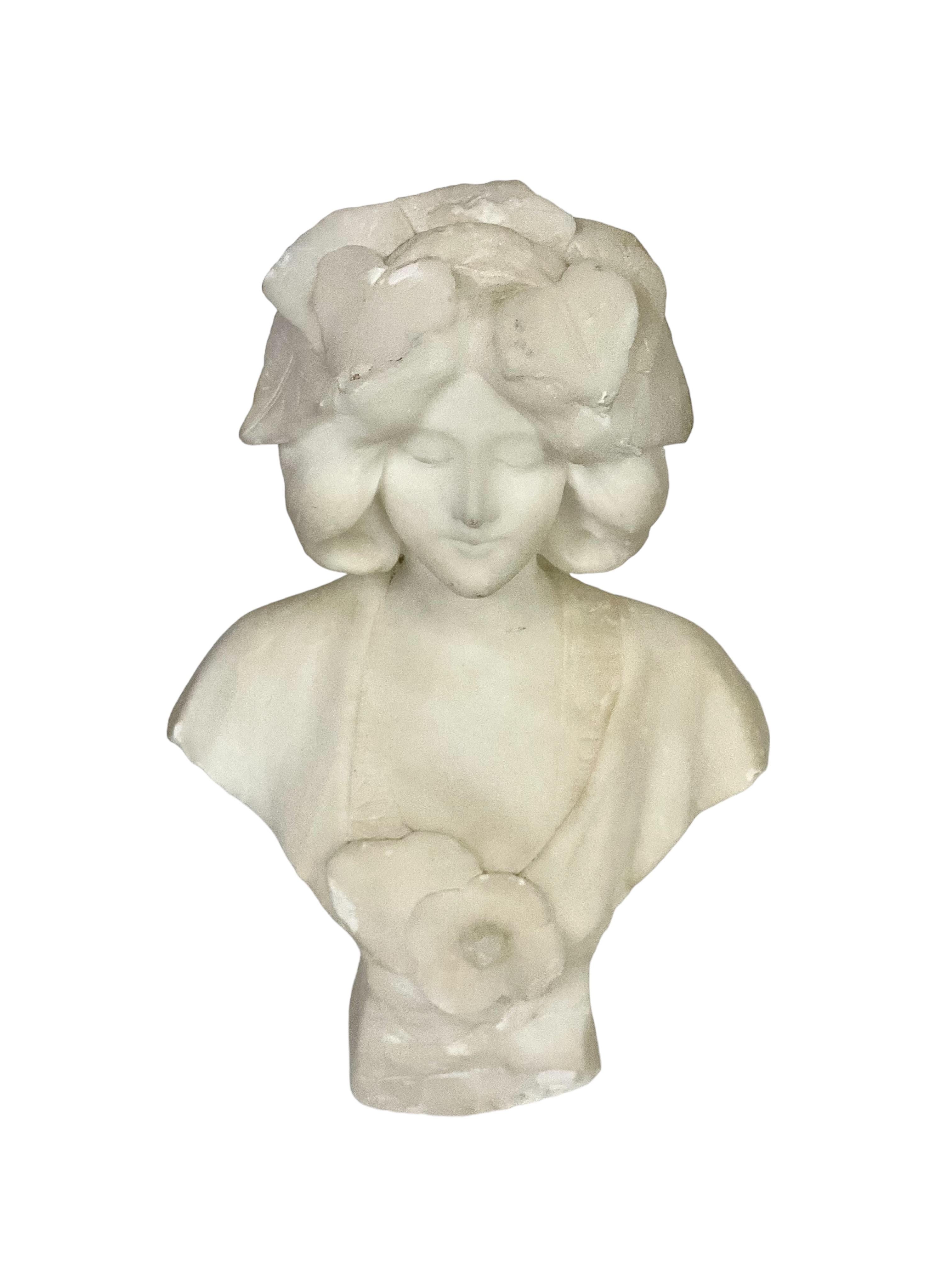 Questo adorabile busto in alabastro di una giovane donna, con i capelli sciolti e ornati da foglie a cascata, emana un'aria di grazia e serenità. I suoi occhi sono socchiusi e il suo viso è espressivo e pacifico, mentre i fiori oversize sul seno