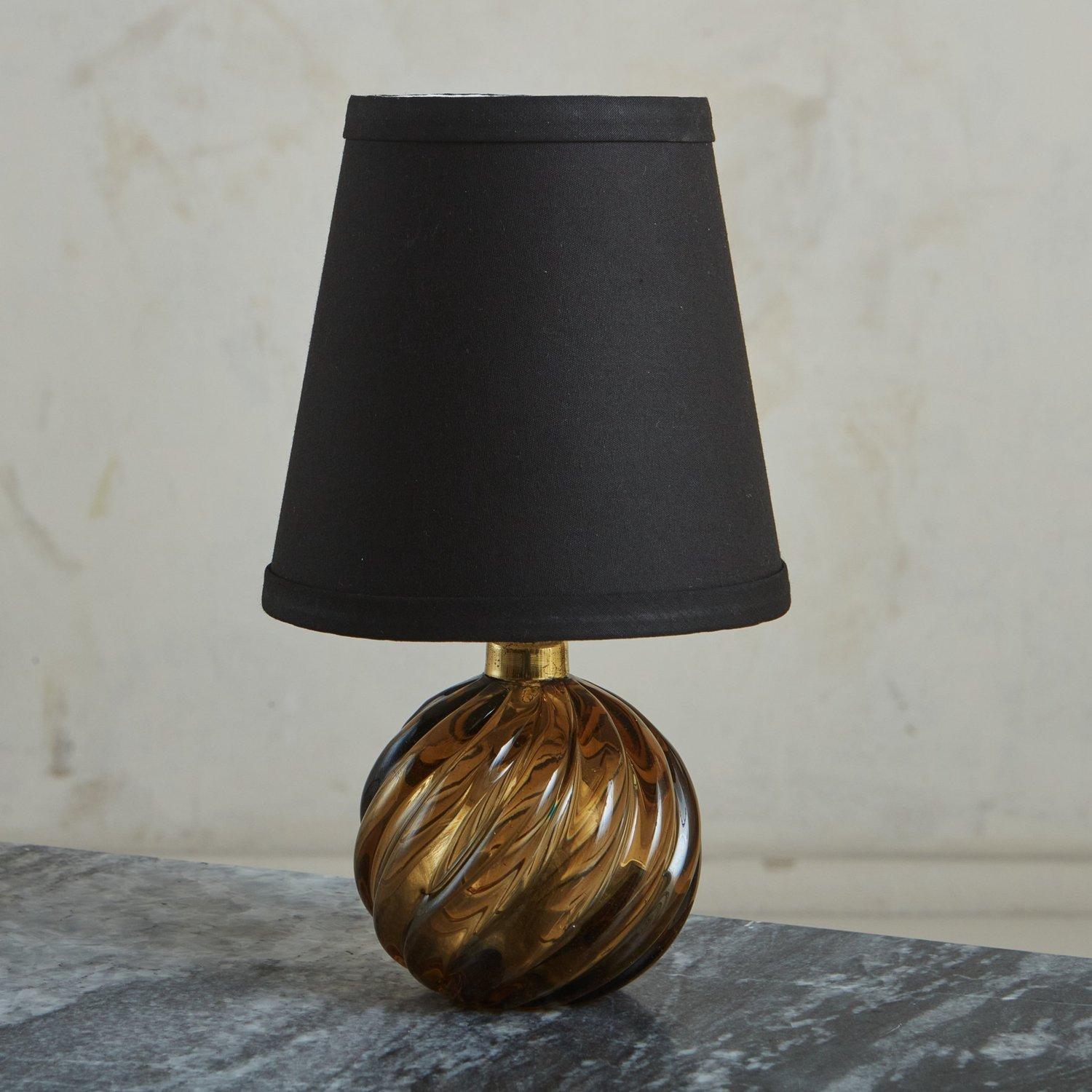 A petite 1930s Italian table lamp by Paolo Venini featuring an amber cased glass body with a brass trim. This lamp includes a new black fabric shade. Acid etched ‘Venini Murano’ stamp on base. Sourced in Italy, 1930s.

DIMENSIONS: 3.75