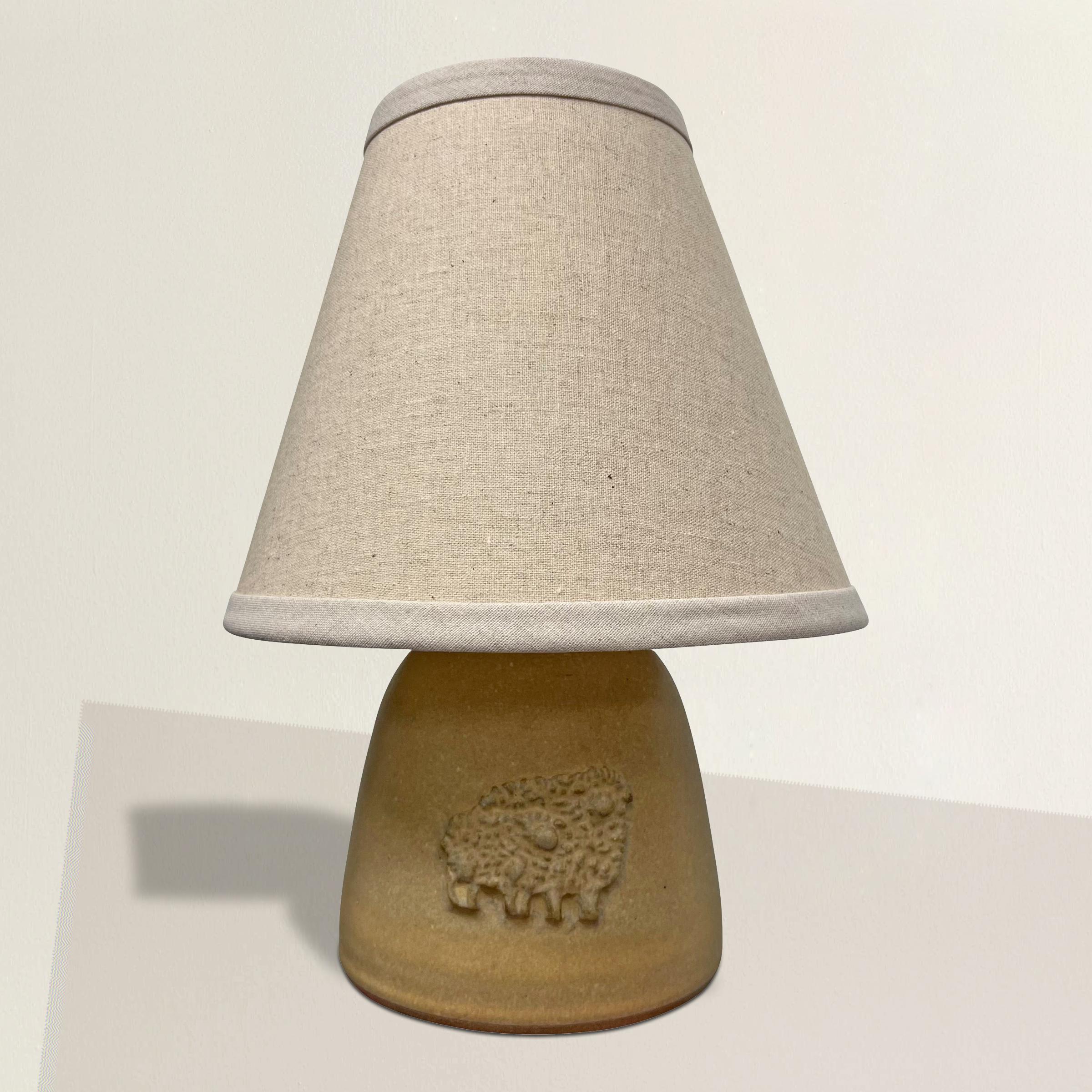 A charming and whimsical petite late 20th century American studio pottery lamp with a pair of sheep applied to the front, and covered in the most perfect brown-mustard glaze, and finished with a new linen shade.  Perfectly at home in your bedroom,