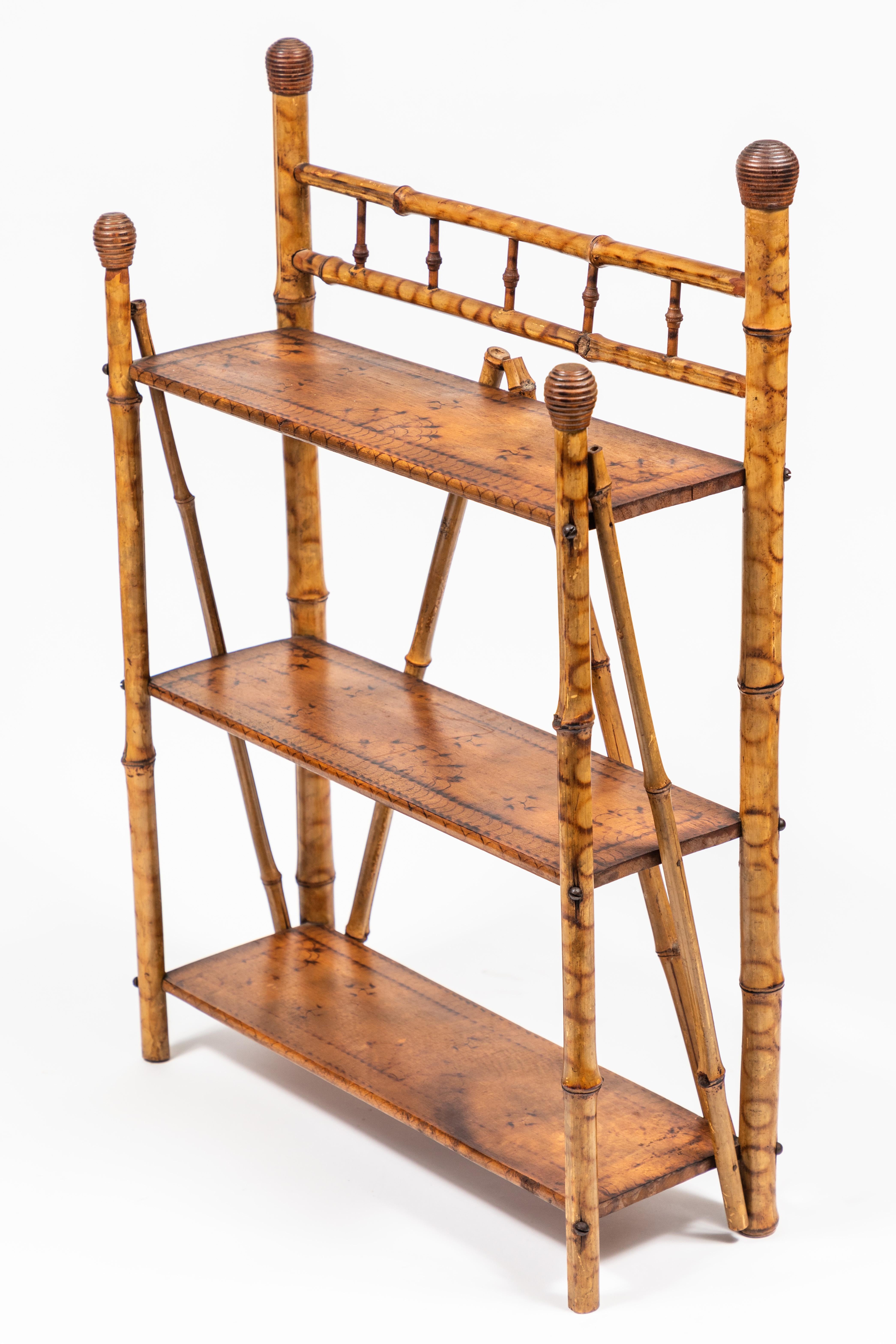 Petite antique bamboo 3-tier standing or hanging shelf.
Posts are topped with carved round finials with ridges. Each shelf is adorned with a hand-done repetitive burn pattern decoration around the edges and in the center.