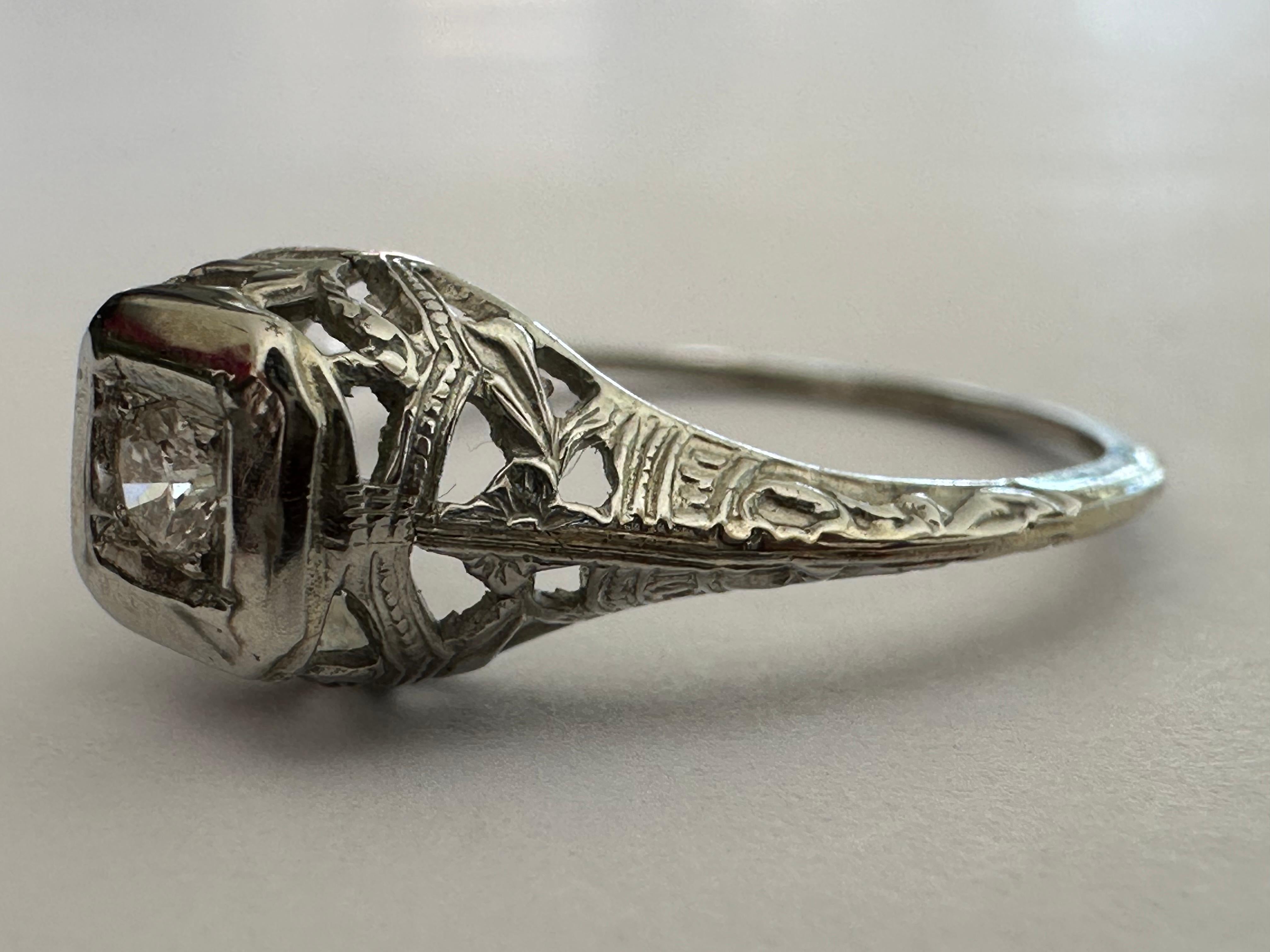 Un diamant de taille européenne ancienne mesurant environ 0,08 carat, de couleur GH et de pureté SI1, brille à l'intérieur d'une monture carrée au sommet d'une monture ajourée en filigrane. Serti en or blanc 18 carats. Circa les années 1920. 

