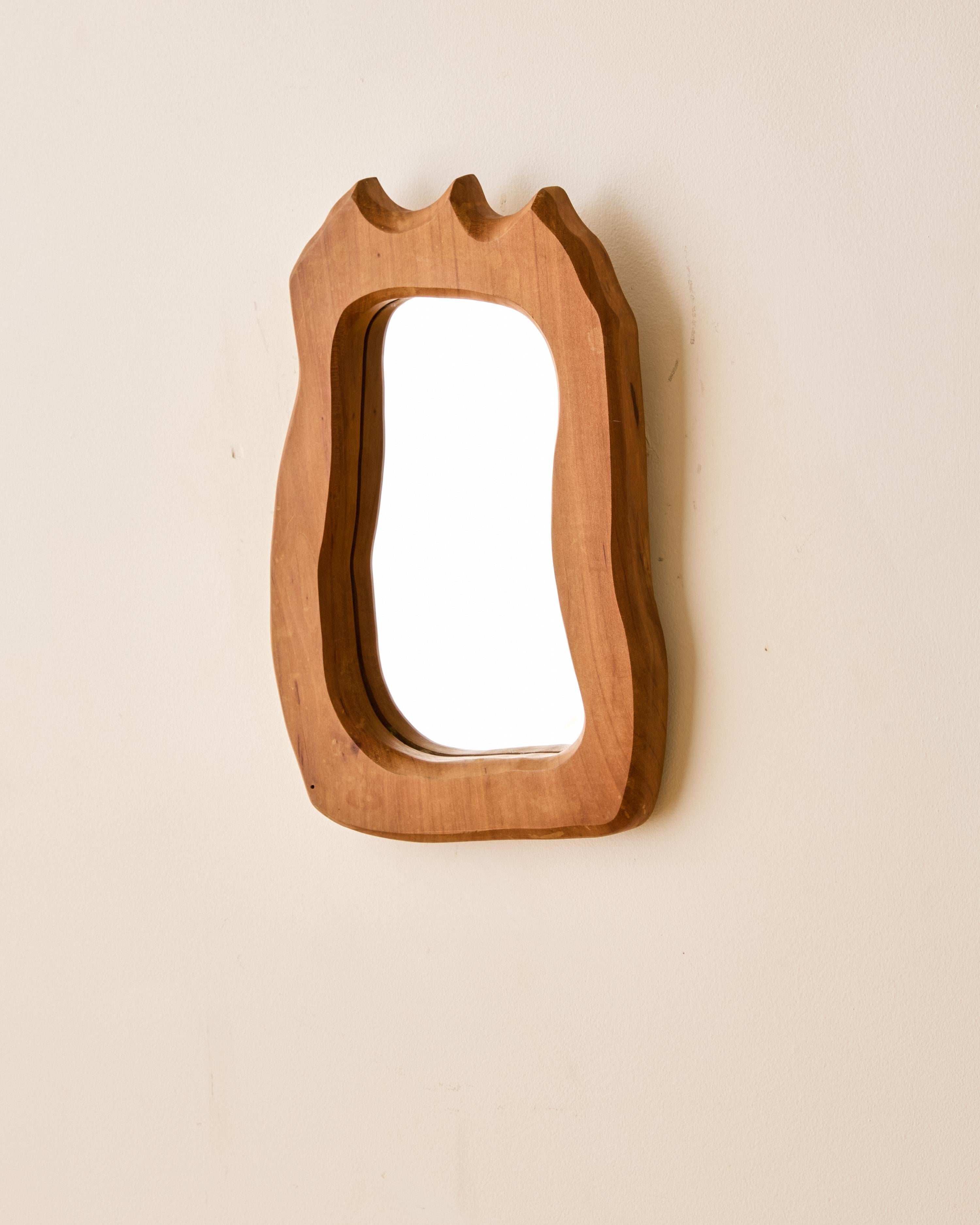 Petit miroir en bois fabriqué artisanalement. Cadre en bois biomorphique et signature au dos. 