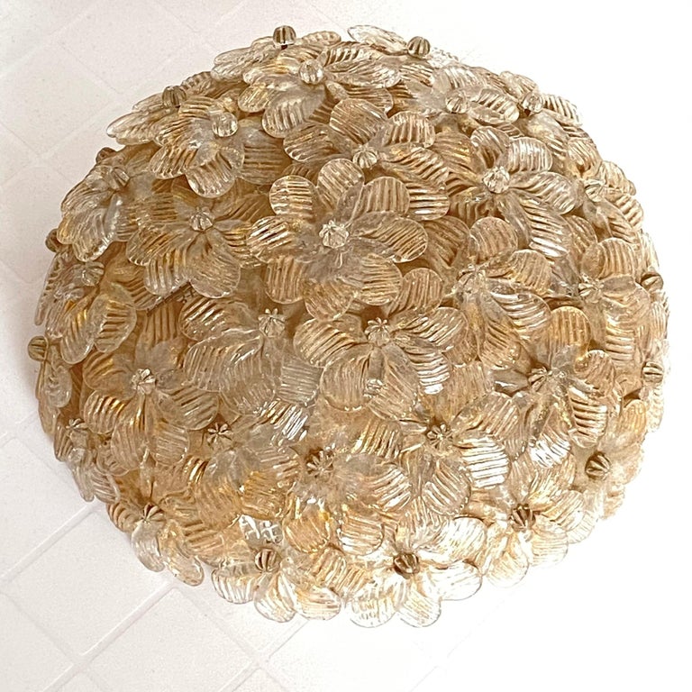 A petite hand blown Italian flushmount chandelier featuring overlapping crystal flowers, gold with 23-carat gold leaf fleck inclusions, mounted on a basket frame. The Fixture requires two European E14 / 110 Volt Candelabra bulbs, each bulb up to 60