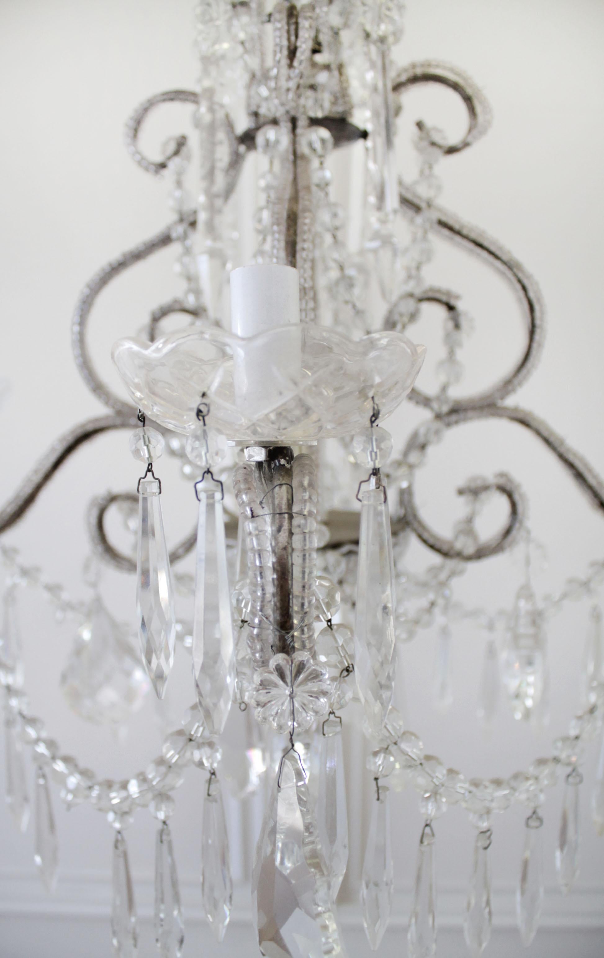 Petite beaded arm silver finish chandelier, with glass bobeche cups, and dainty rosettes. Crystal spear type crystals suspend from each garland adding a little extra sparkle.
Size: 22