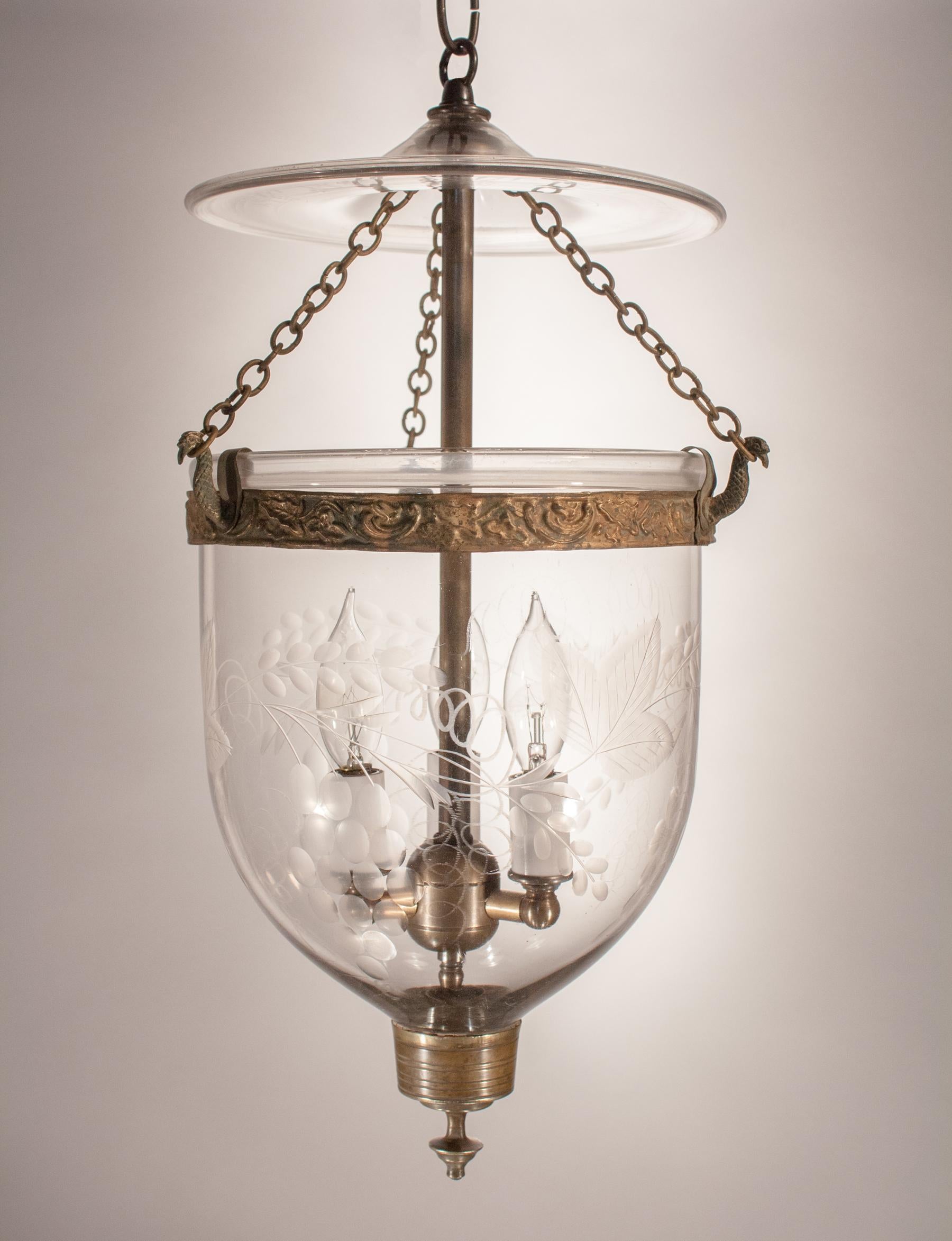 A charming 19th century bell jar lantern with etched grape and leaf motif. This circa 1880 petite pendant features a period embossed brass band and finial candleholder base. The quality of the hand blown glass is excellent, with desirable swirls in