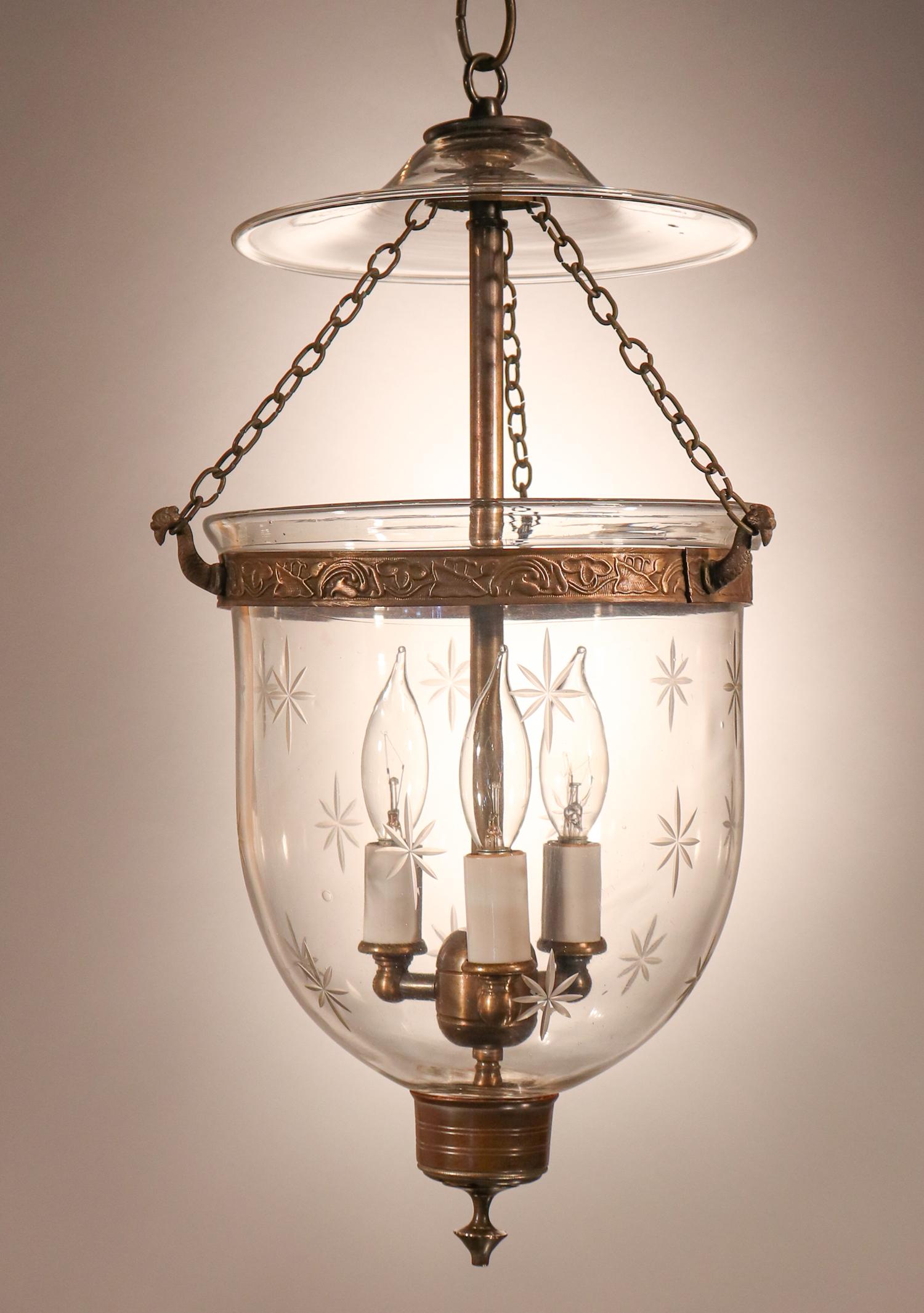 An antique English bell jar lantern with lovely form complemented by a finely etched star motif. This petite, circa 1890 pendant features very good quality hand blown glass complemented by an embossed brass band and simple candleholder base with