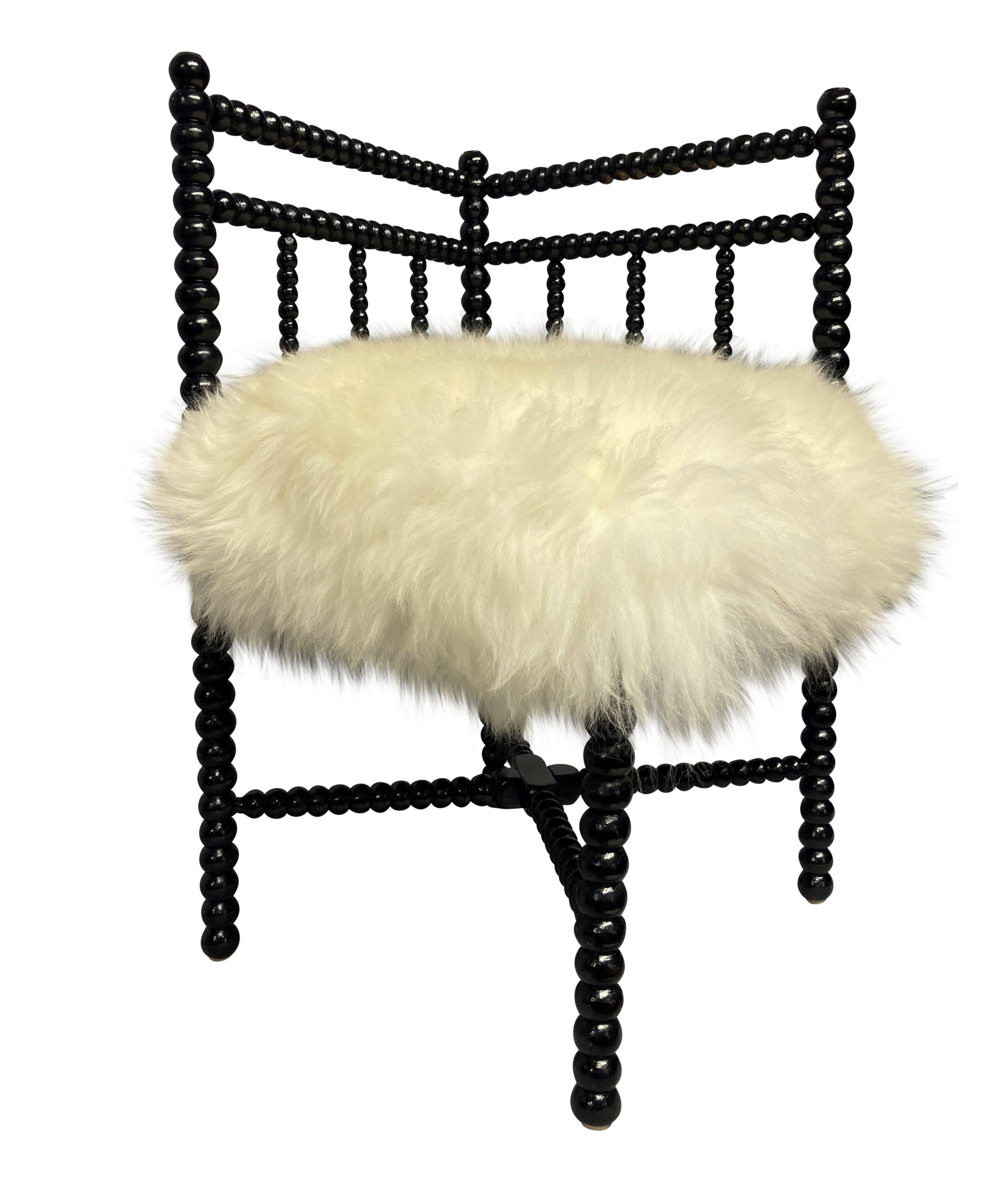 A petite English black lacquered corner bobbin chair, upholstered in sheepskin.