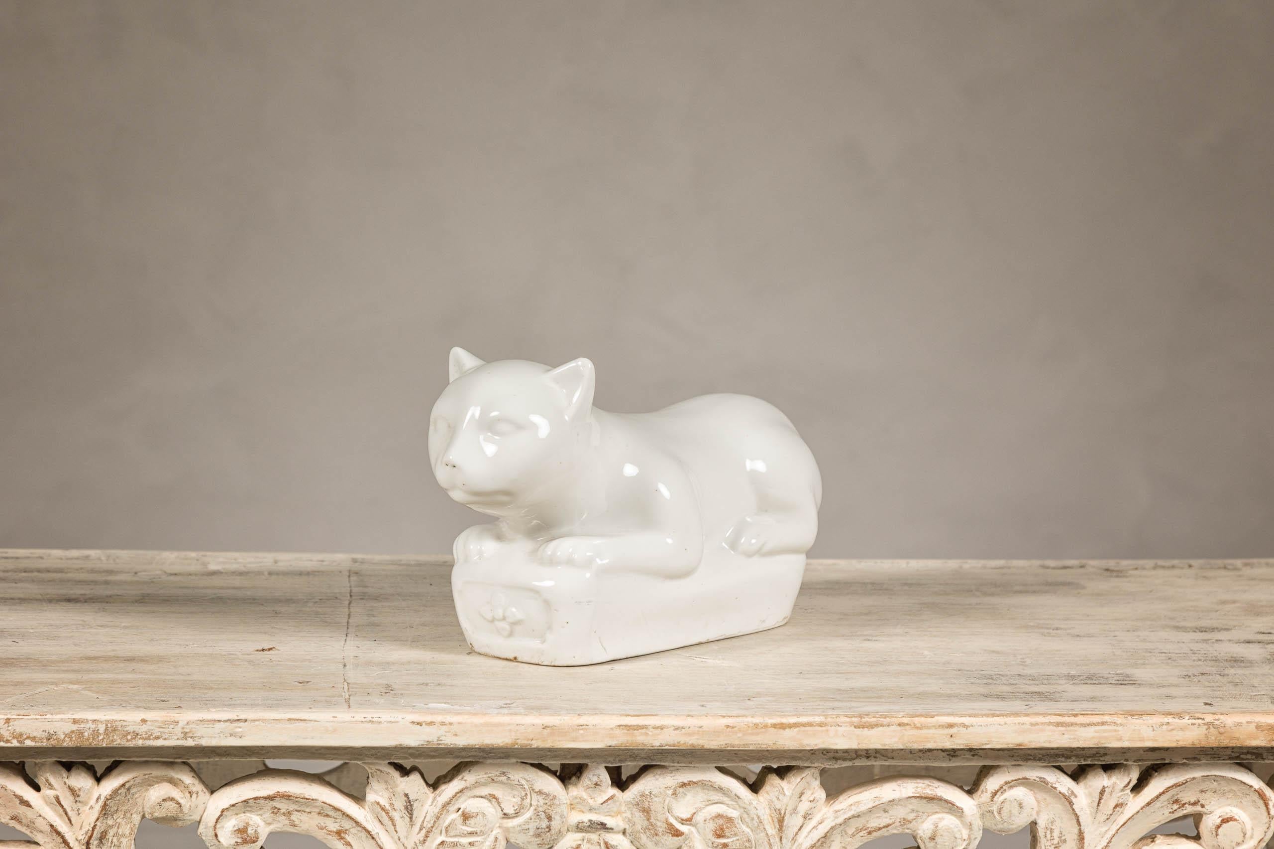 This petite vintage Blanc de Chine porcelain cat is a charming and elegant decorative piece that captures the serene beauty of a cat in repose. Crafted with meticulous attention to detail, this figurine portrays a cat lying gracefully on a base that
