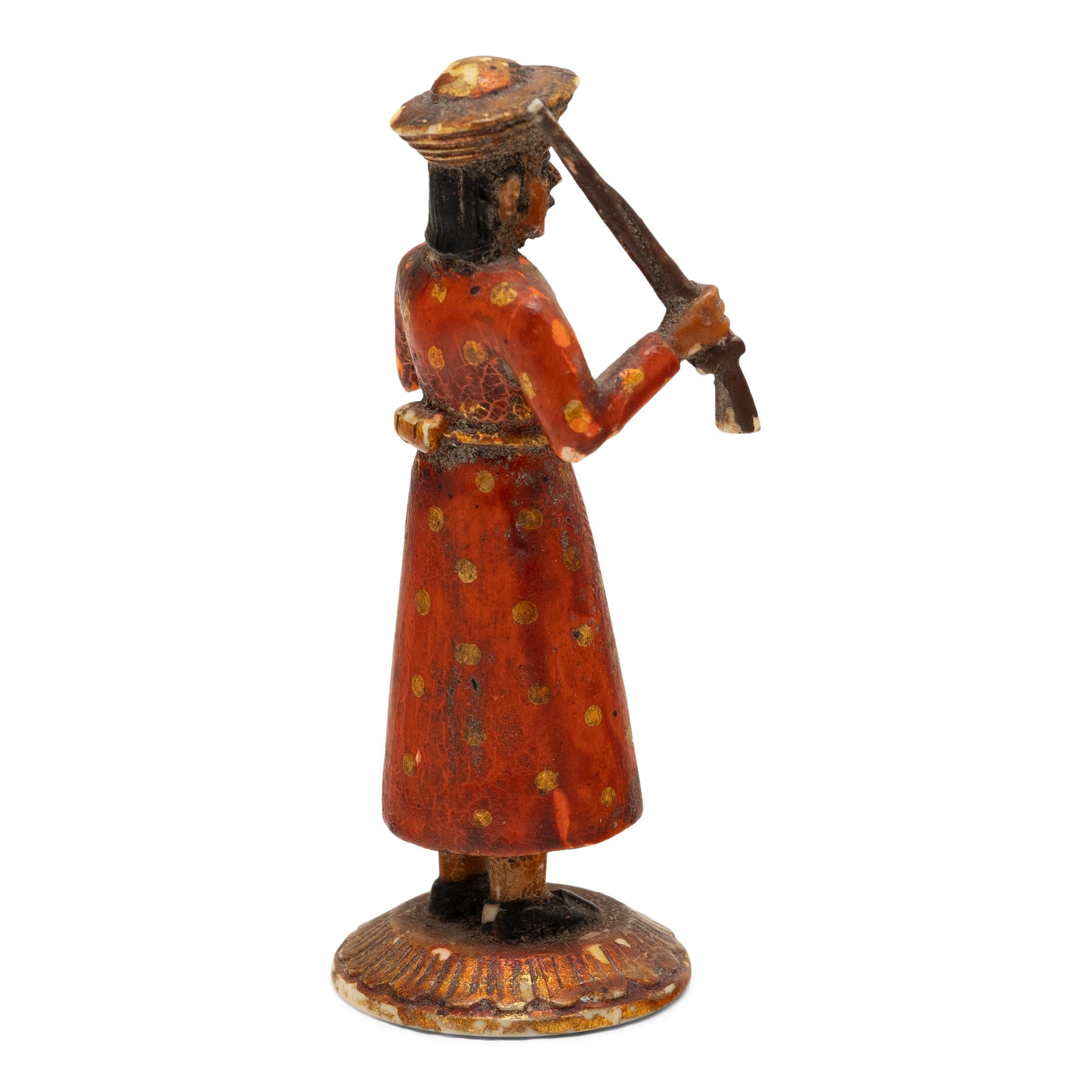 Cette figurine du début du XXe siècle est sculptée à la main dans de l'os et représente un soldat indien tenant un fusil à mousquet. Inspirée des cavaliers Sowar qui servaient sous la Compagnie britannique des Indes orientales, la petite figurine