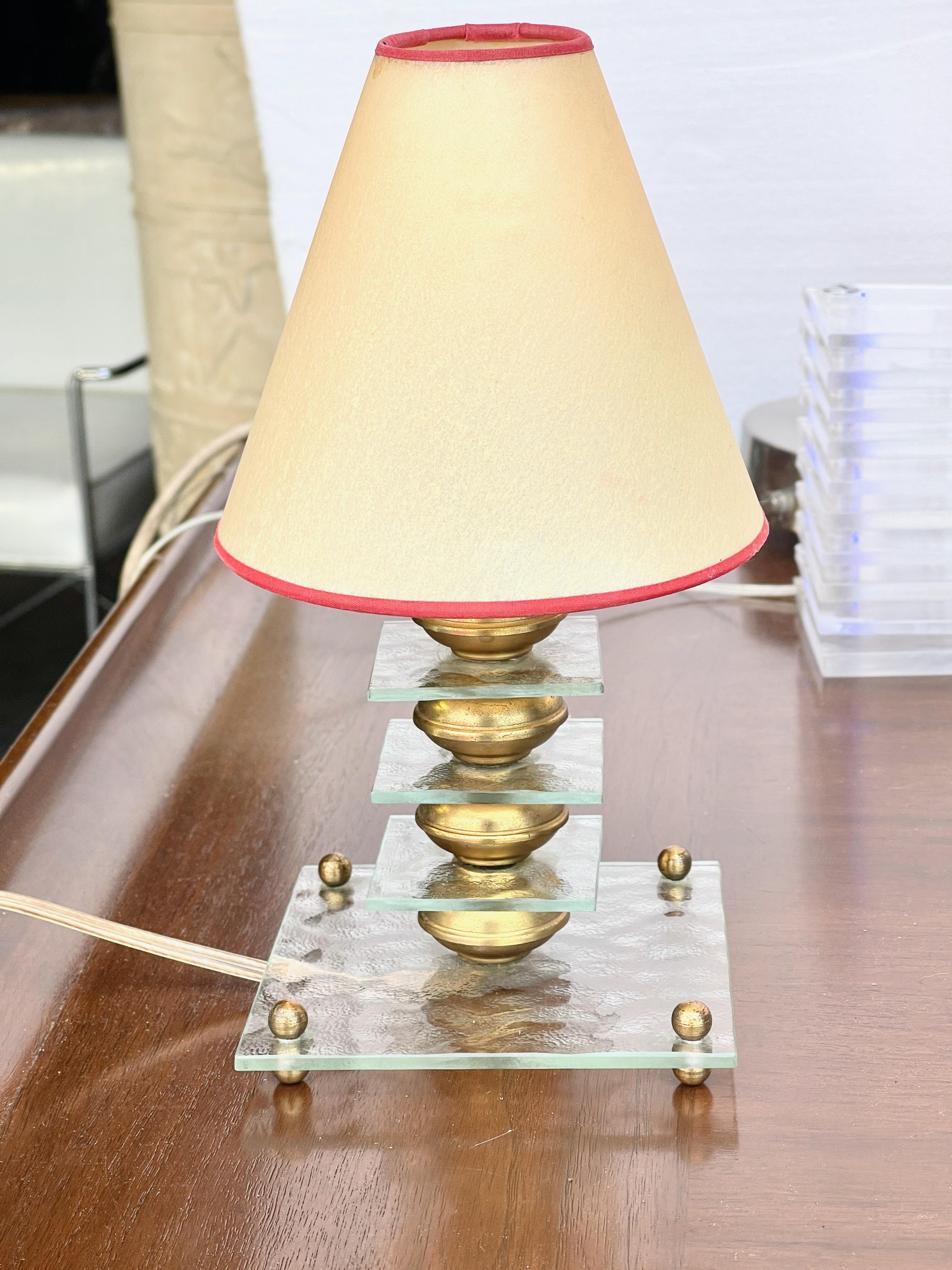 Adorable petite Art Deco boudoir table lamp in the style of La Maison Desny made of stacked squares of rippled glass separated by brass tangerine shaped spacers on a larger square glass base on four double brass ball feet.
Shown with original brass