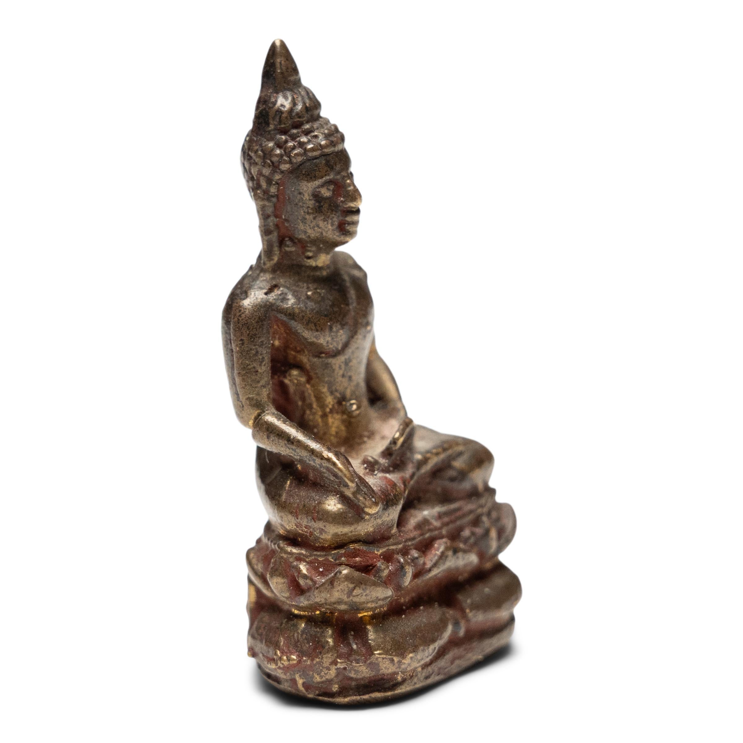 Dieses zierliche thailändische Gebetsamulett stellt einen sitzenden Medizinbuddha dar, der auch als der König der Heiler bekannt ist. Der zierliche Buddha ist aus Messing gegossen und mit Spuren von roten und goldenen Pigmenten versehen. Er sitzt in