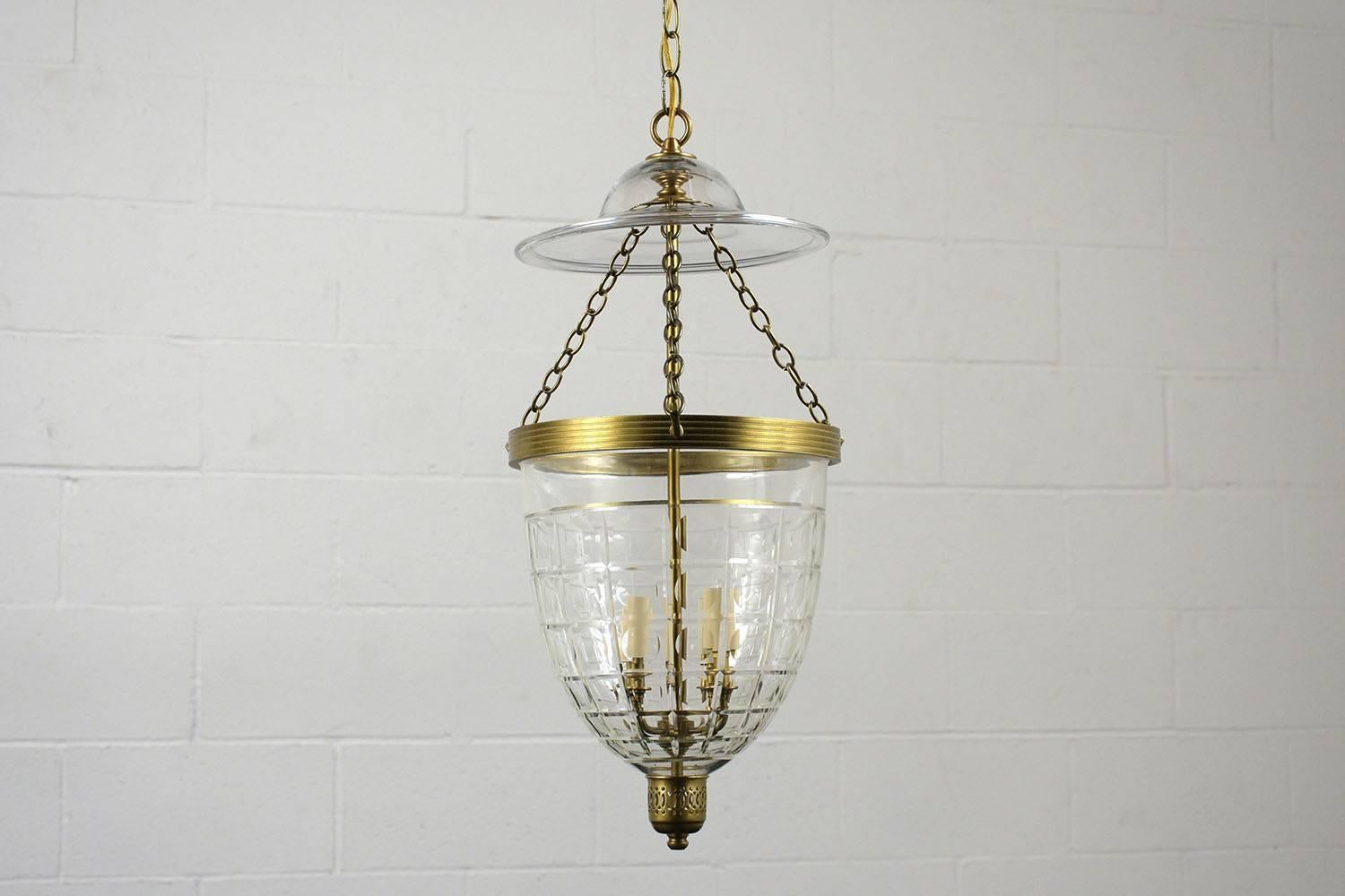 This 1980s Regency-style pendant lantern has a cut glass shade with a square design and brass accents along the top and bottom. Inside the shade are four lights with faux candle covers. The chain is 12 inches long with a glass top shade. This
