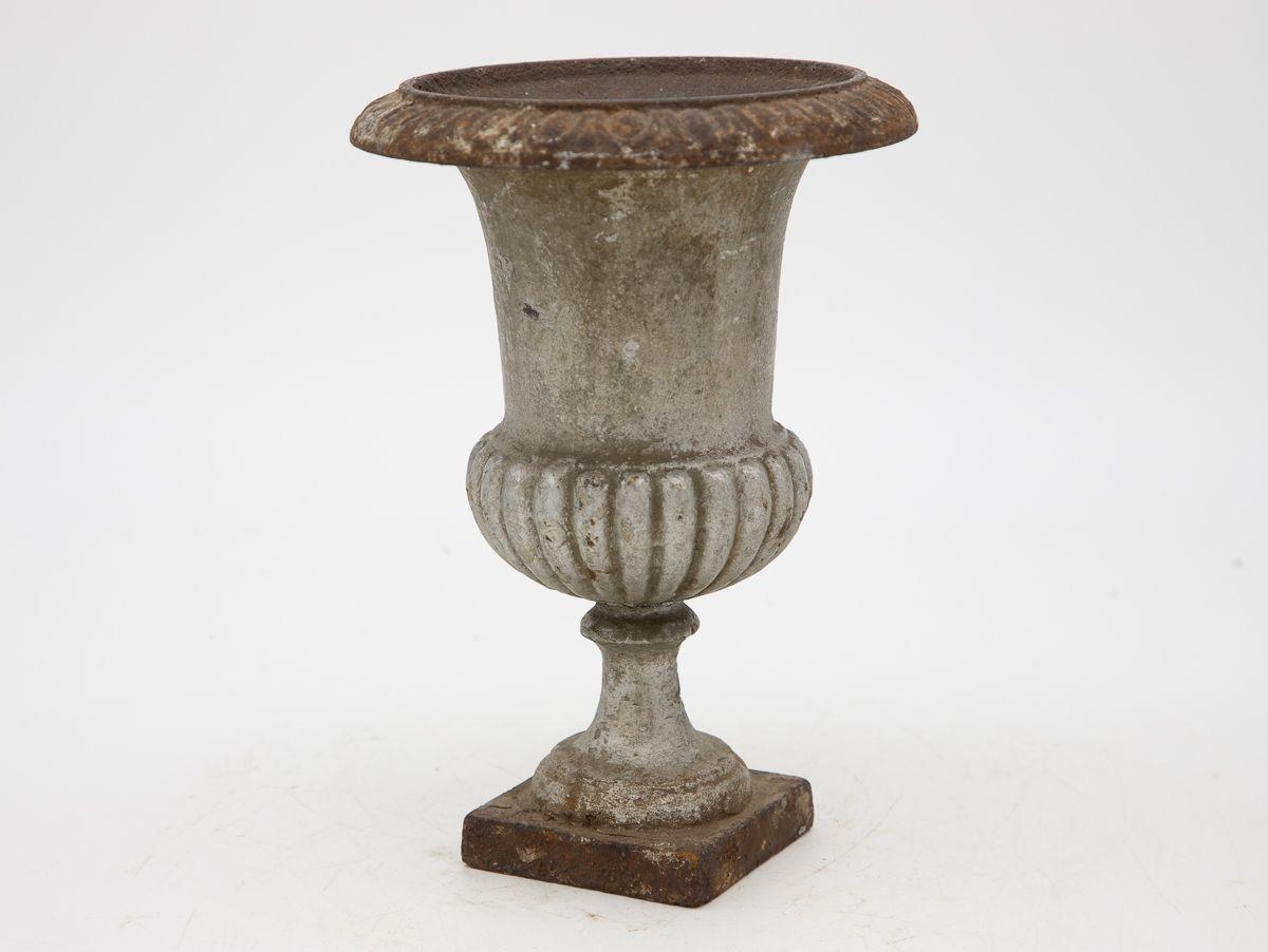 A mid-20th century grey slightly metallic painted cast iron urn. This urn features an egg and dart pattern on the top rim and a fluted bottom on a square base. Some paint loss, rust spots, wear consistent with age and use.