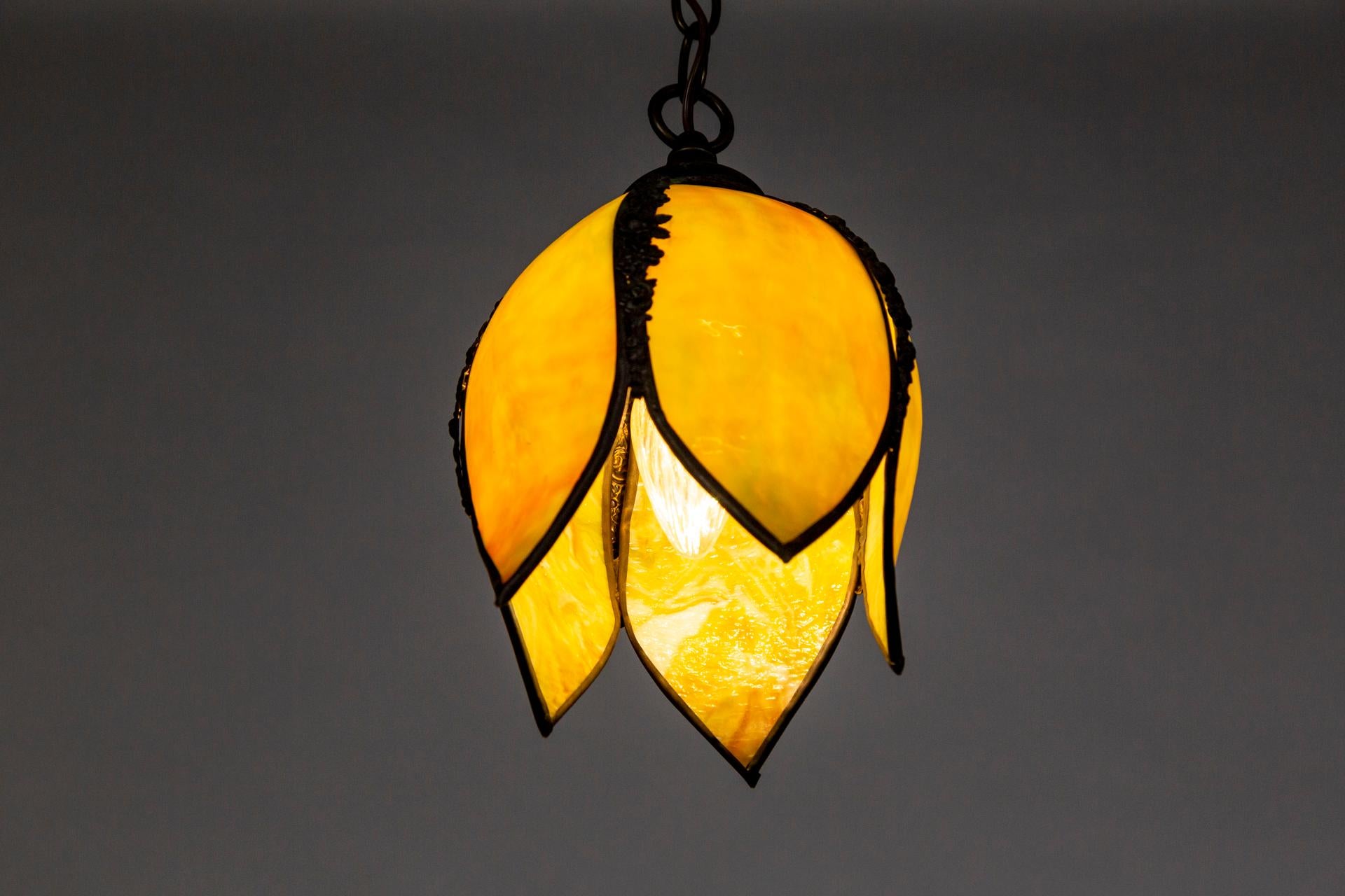 A petite, chartreuse, slag glass hanging light in a tulip shape. It changes to a yellow tone when lit. The 5 petals are lined with floral, cast metal trim in a dark patina. With a new, darkened brass chain and canopy. Mid-20th century. Newly wired.