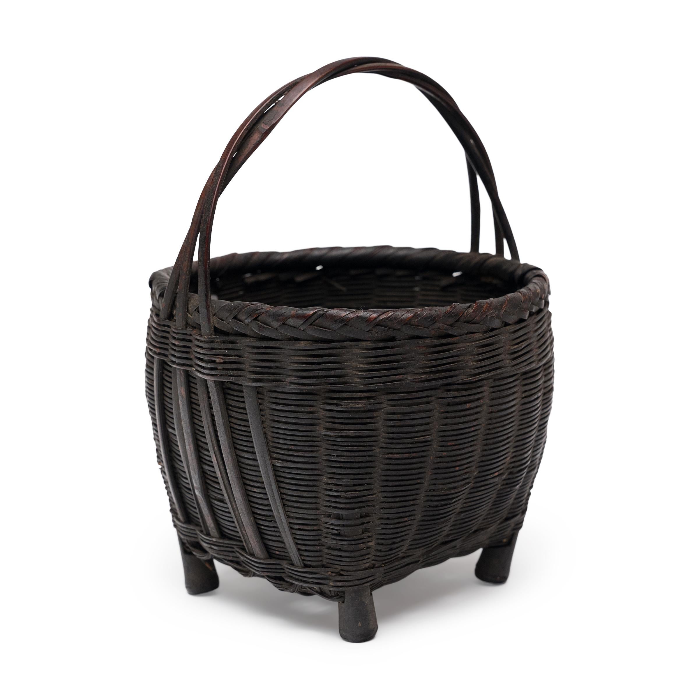 Woven with precious scale and delicate artistry, this petite flower basket from the early 20th century is a lovely example of traditional Chinese basketry. The small basket is woven of thin strips of lacquered bamboo, shaped with a square-to-round