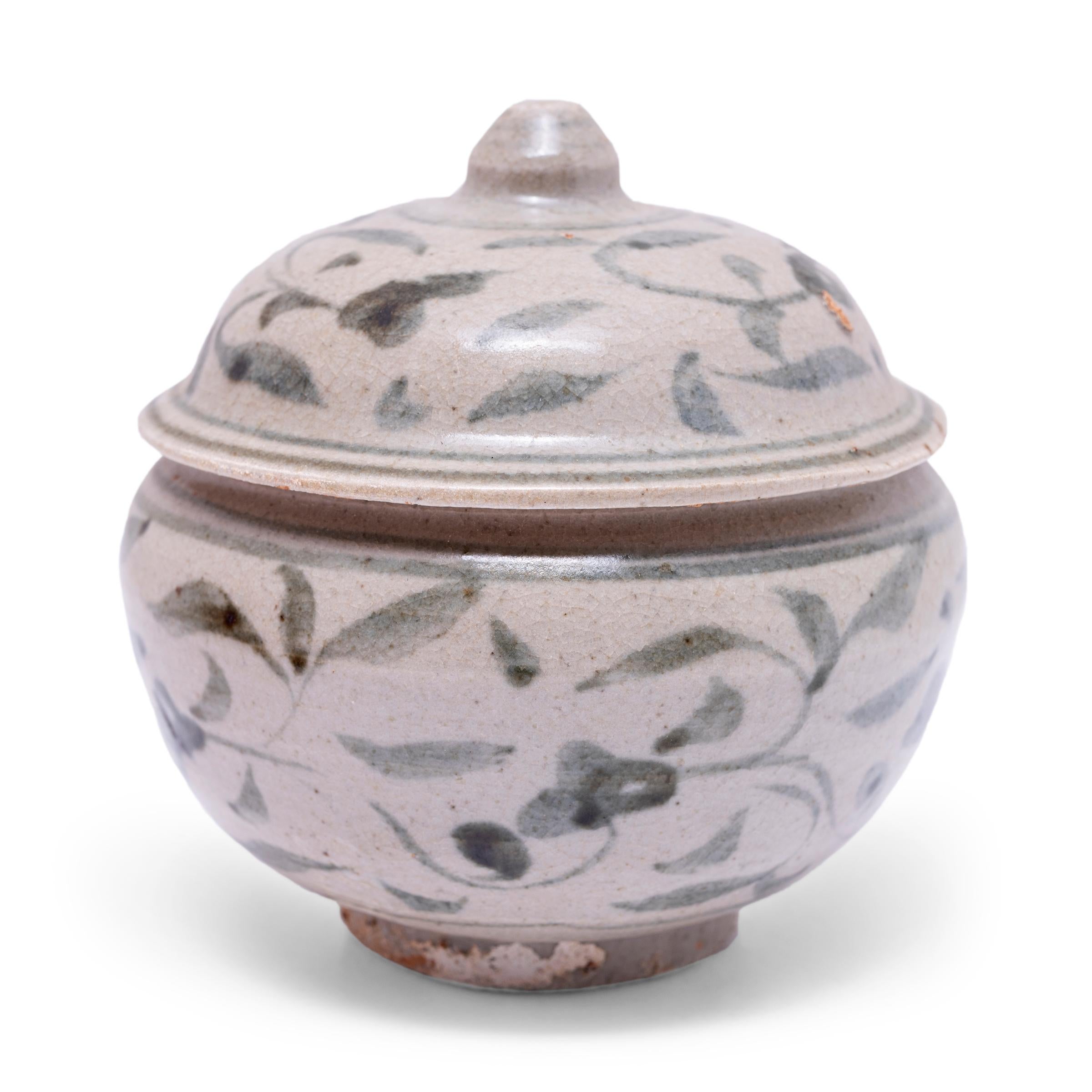 A charming example of provincial blue-and-white pottery, this petite lidded jar from the late Ming dynasty (1368-1644) is cloaked in a cool grey underglaze and decorated with expressive dark blue brushwork of abstract florals. The jar has a rounded