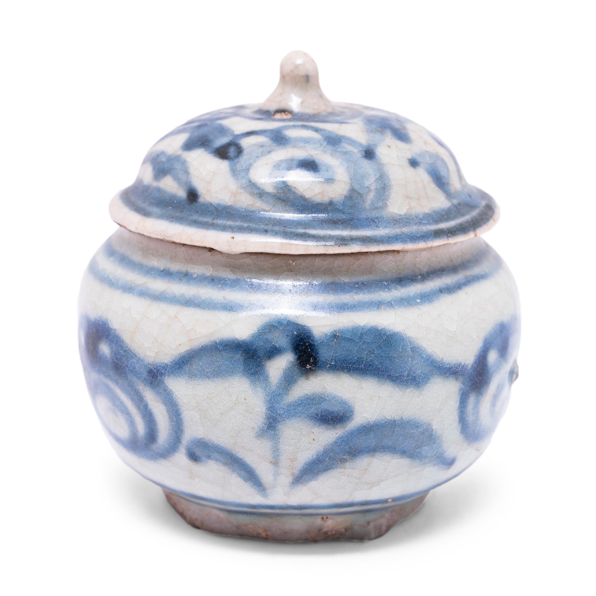 A charming example of provincial blue-and-white pottery, this petite lidded jar from the late Ming dynasty (1368-1644) is cloaked in a cool white underglaze and decorated with expressive blue brushwork of abstract florals. Shaped with a round body