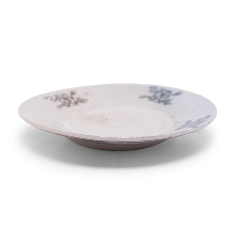An everyday example of Chinese blue-and-white porcelain, this petite footed dish charms with expressive cobalt-blue decoration, sparsely brushed atop a blue-grey underglaze. The gently tapered sides are patterned with a ribbon-clad hundred antiques