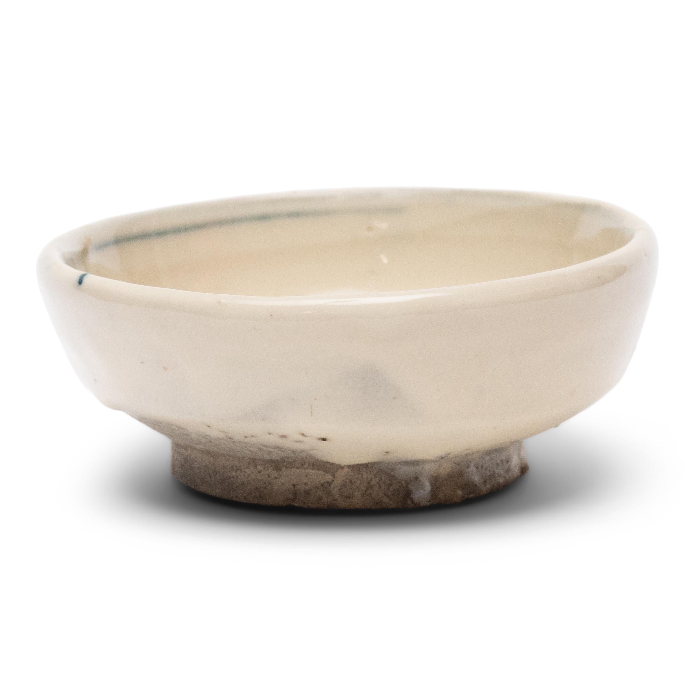 An everyday example of Chinese blue-and-white ceramics, this petite footed dish from the late Qing dynasty is appreciated for its refined simplicity and charming imperfections. The small bowl is cloaked in a thick, crème-white glaze and decorated