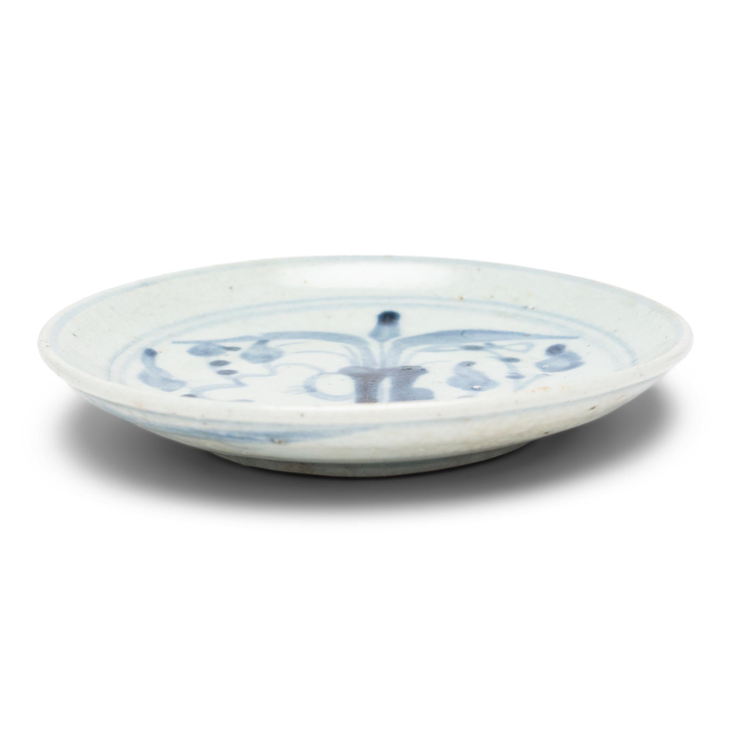 An everyday example of Chinese blue-and-white ceramics, this petite footed dish from the late 19th century charms with expressive sweeps of cobalt blue atop a blue-grey field. The loose brushwork likely depicts a lotus plant emerging from murky