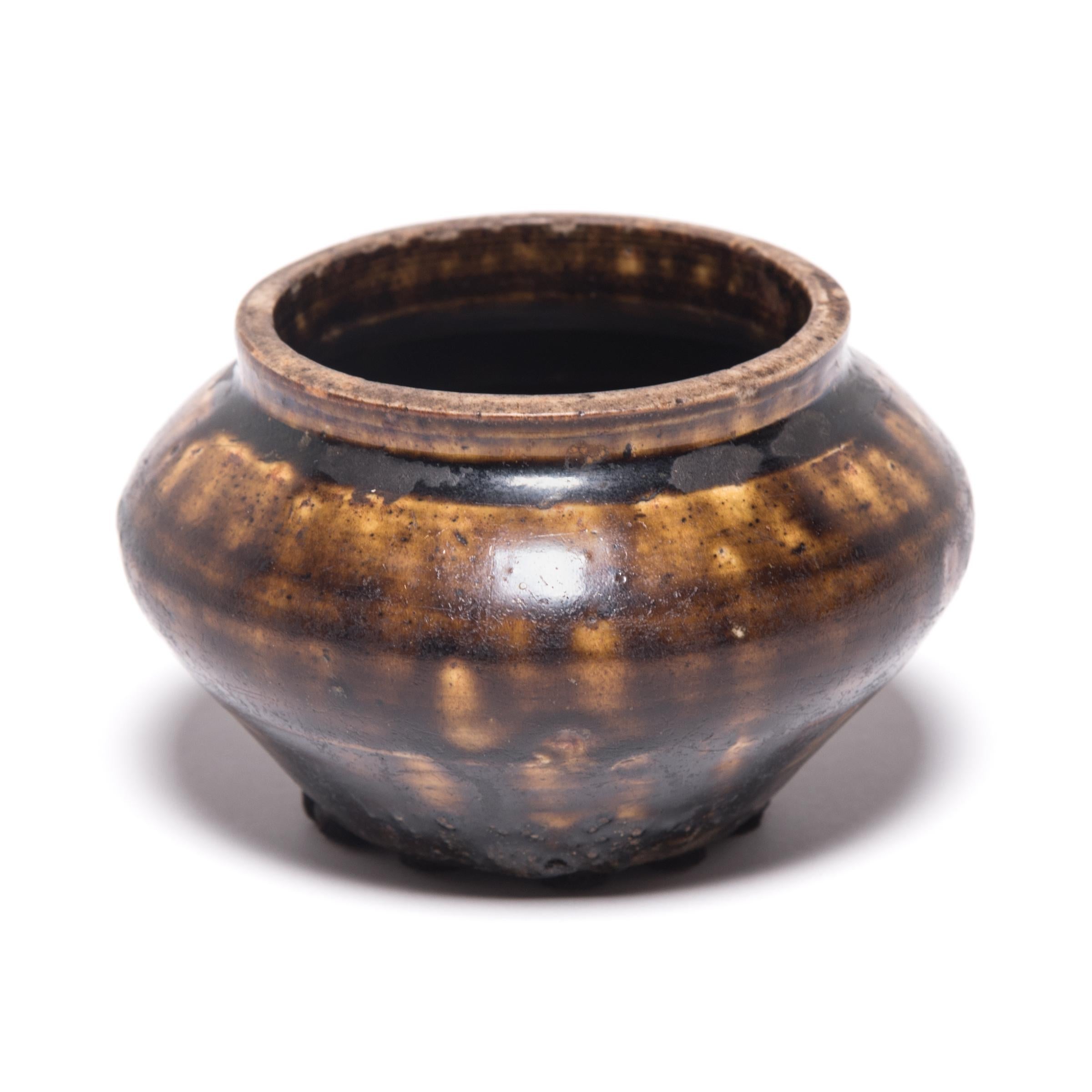 Based on forms tracing back to the Han dynasty, this 19th century vessel emulates the full-bodied shapes and unusual glazing found in ancient ceramics. Marked with barren spots, a rich, brown glaze clings to the pot’s broad shoulders, pooling