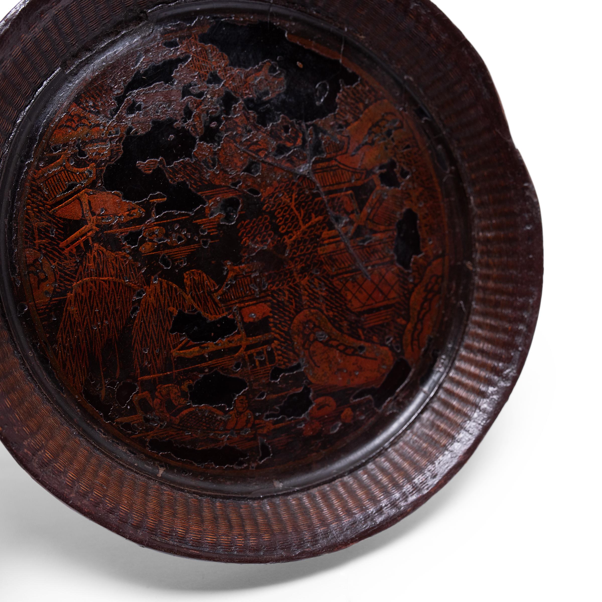 Dated to the mid-19th century, this small, round tray was likely once used as a shallow offering bowl atop a home altar. Comprised of finely woven bamboo sides and a thin wooden base, the plate is coated with dark black lacquer and decorated with a