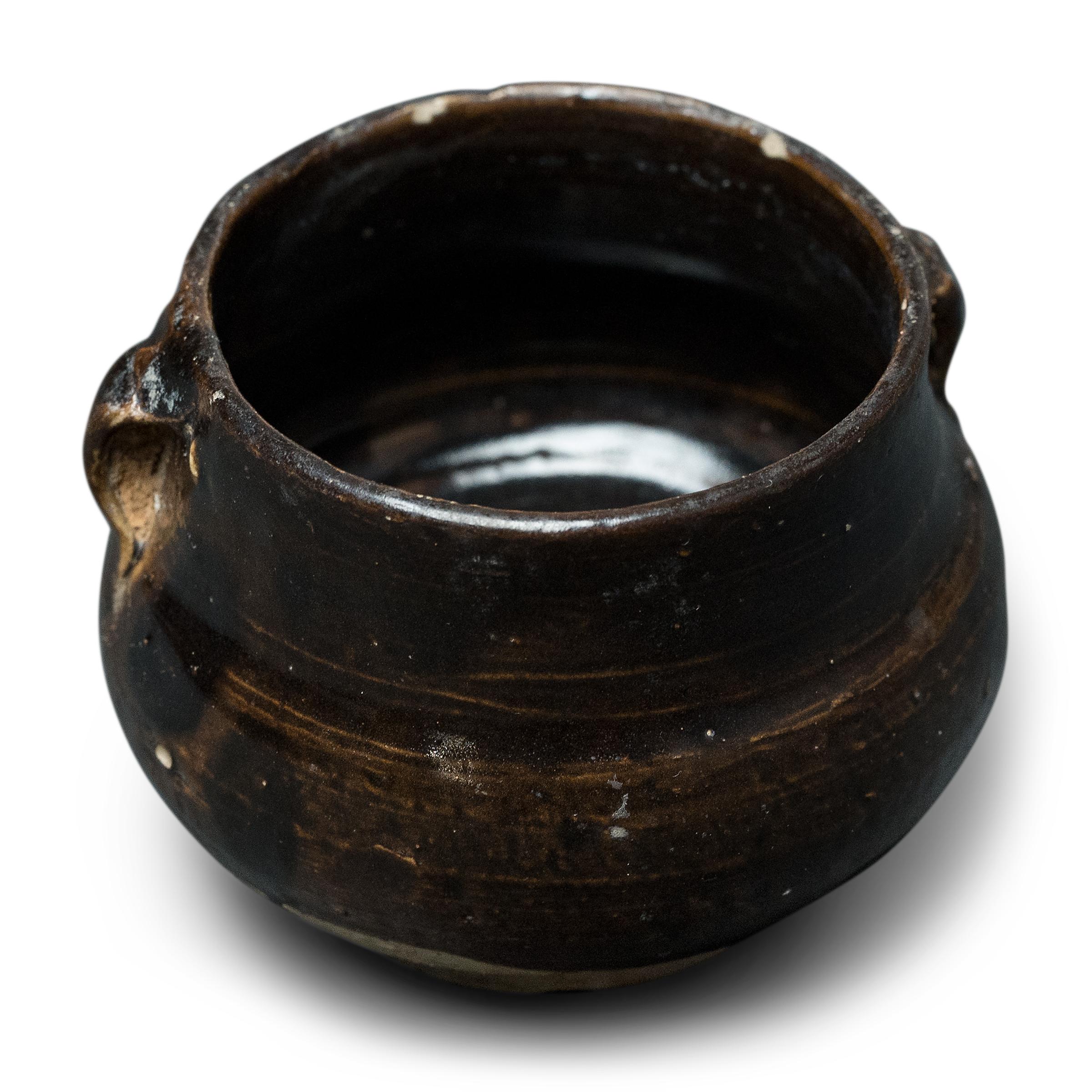 Questo piccolo vaso smaltato proveniente dalla provincia cinese dello Shanxi esemplifica il fascino senza tempo della ceramica artigianale. Un tempo utilizzato in spezieria per contenere erbe e oli macinati per le medicine tradizionali, il vasetto