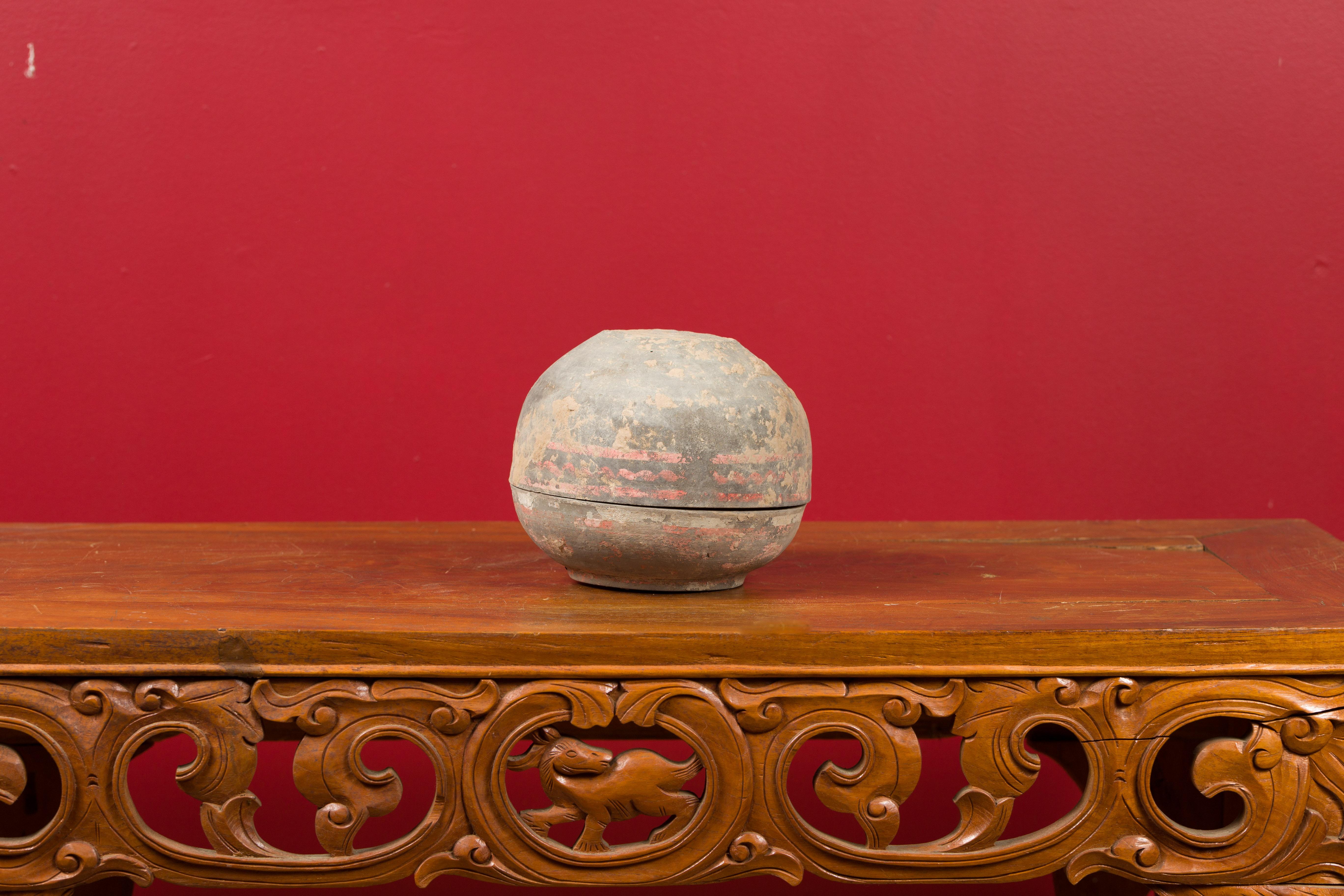 A petite Chinese Han dynasty circular lidded vessel with traces of original paint, circa 202 BC-200 AD. Handcrafted in China during the prestigious Han dynasty, this small terracotta vessel features a circular shape topped with a matching lid.