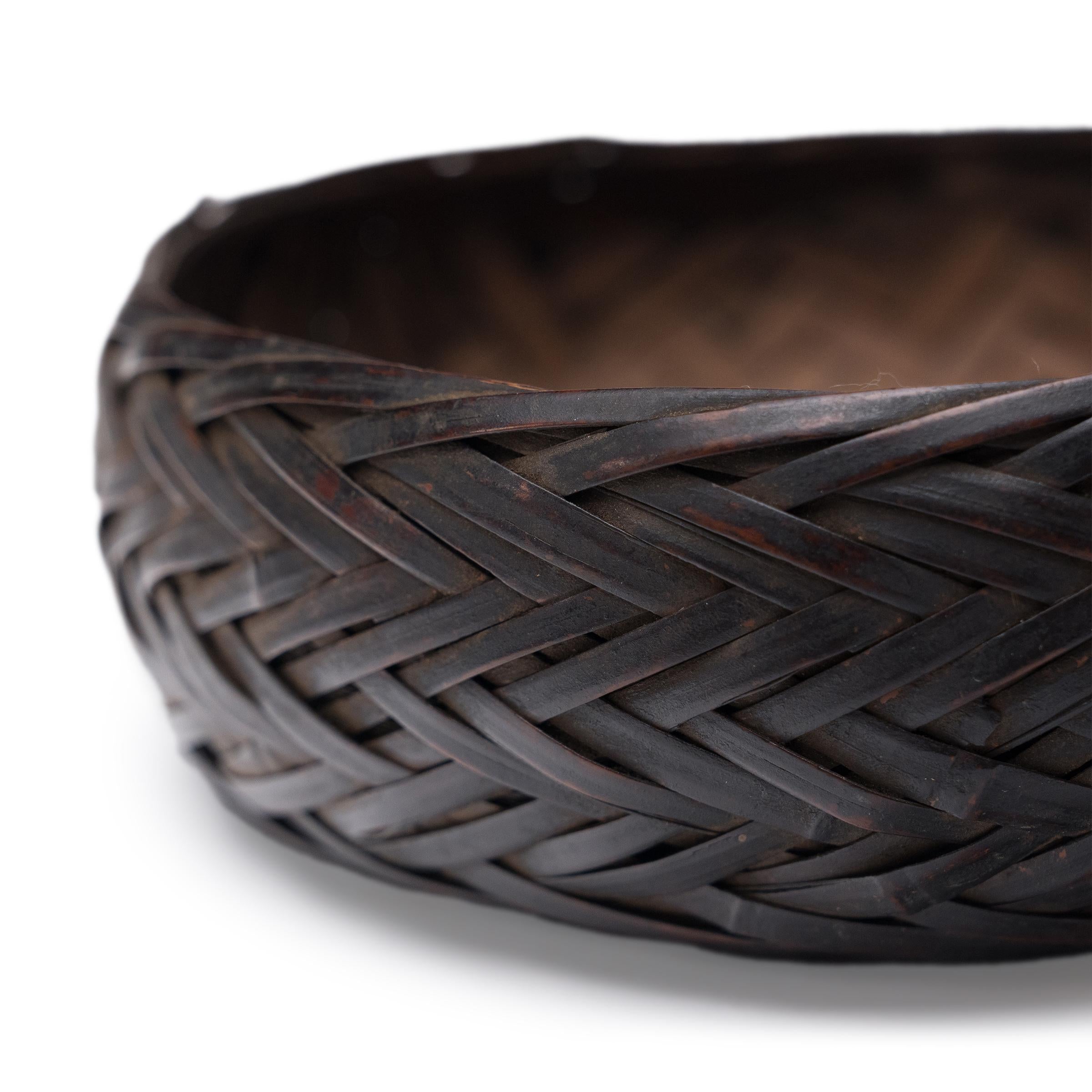 Questo cesto intrecciato proveniente dalla provincia di Guizhou celebra la splendida semplicità di un oggetto intrecciato a mano. Sapientemente intrecciato con sottili strisce di bambù, il piccolo cestino veniva originariamente utilizzato per