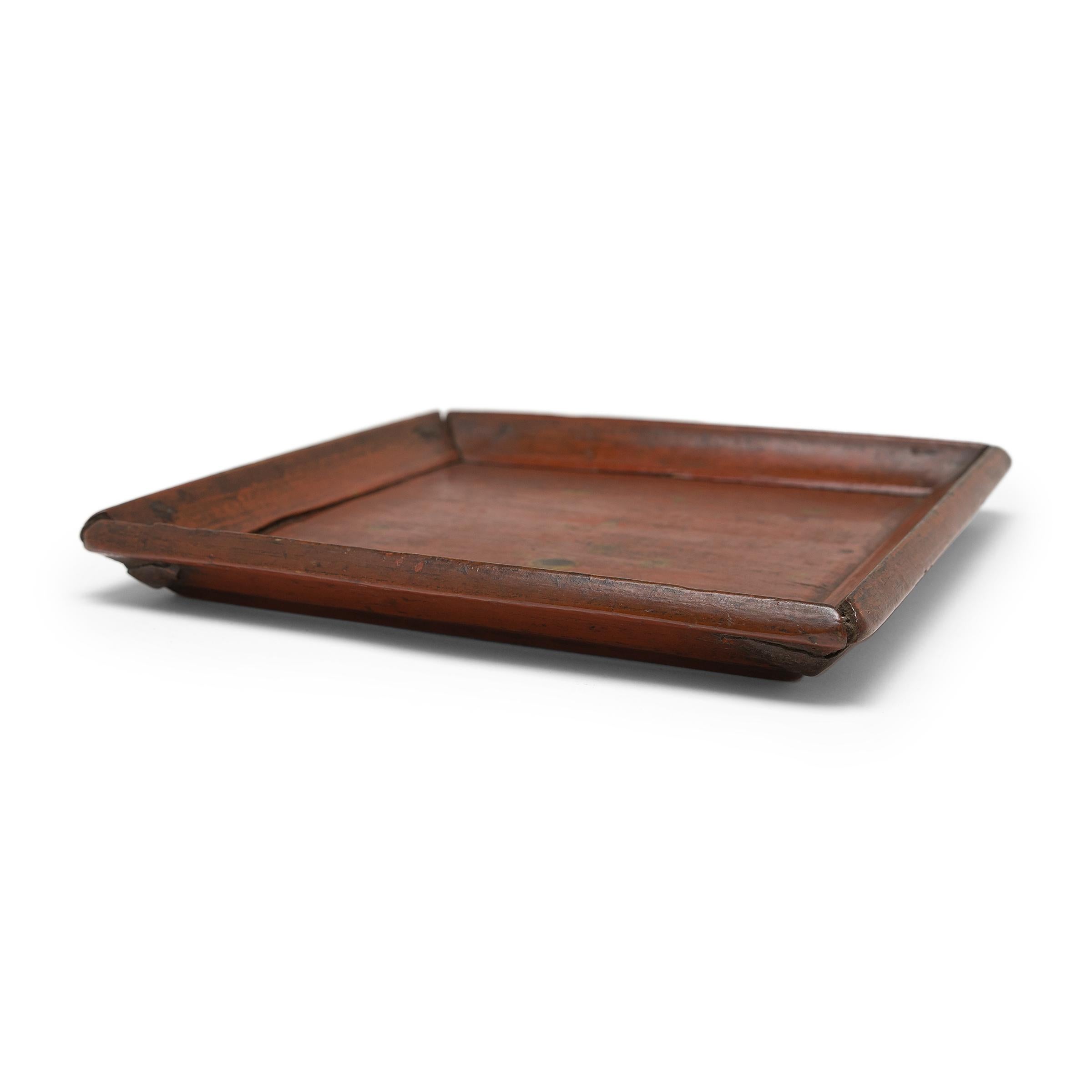 Simple lines, a modest form, and a layer of hand-brushed lacquer give this petite Qing-dynasty tray a provincial charm that recalls the warmth of home. The red lacquer finish has weathered with time slightly revealing the light brown coloring of its