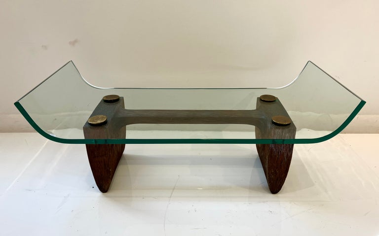 Unusual and beautifully carved and constructed coffee table. The trestle base is intricately channel and chip carved, mounted with upward curving glass top secured by large brass caps. 

Unmarked but attributed to Aldo Tura. Total height is