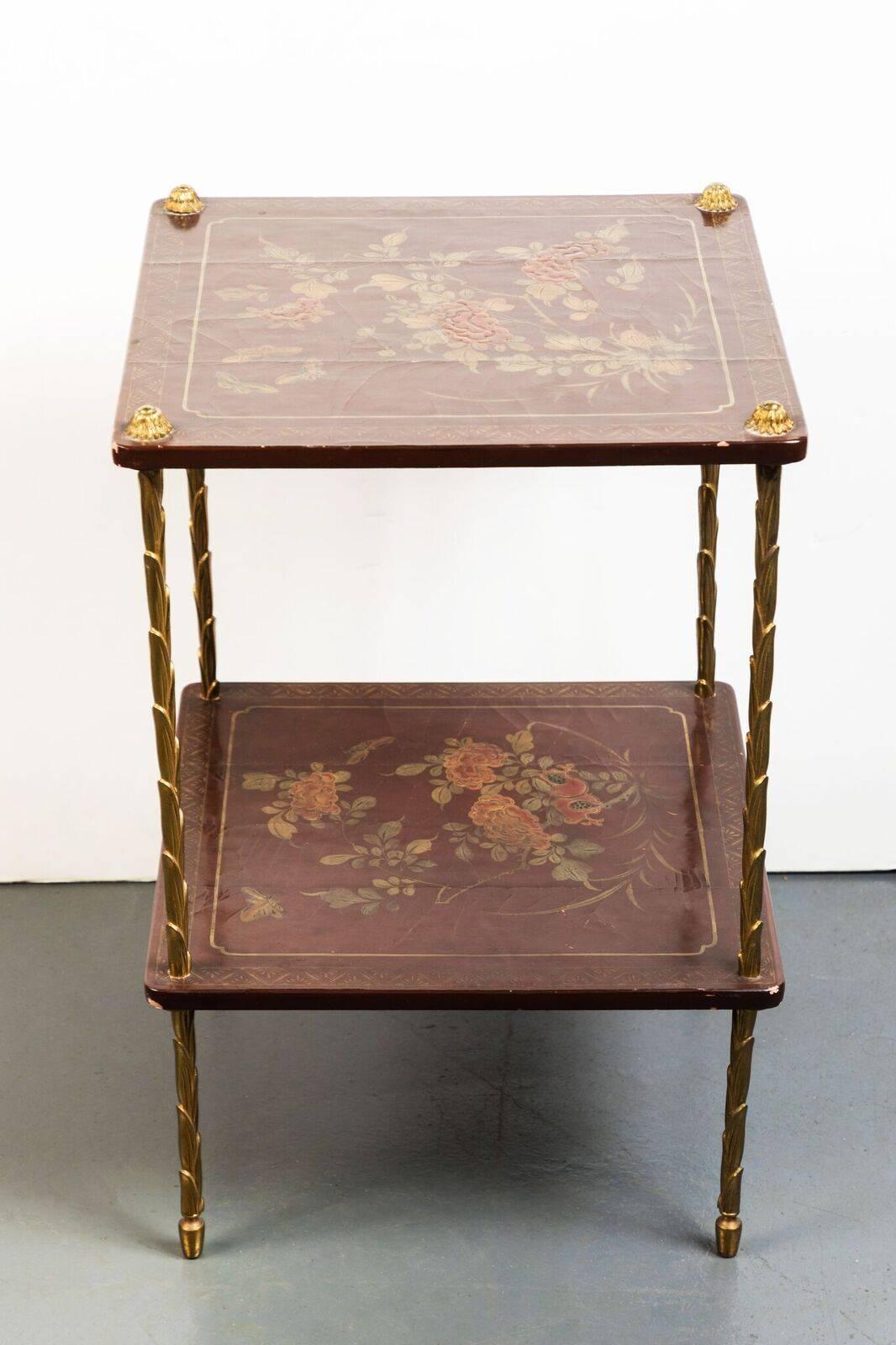 Pair of charming, hand-painted and lacquered, parcel-gilt, two tier, English, chinoiserie side tables in oxblood. Each standing on brass legs in a stylized, foliate design.