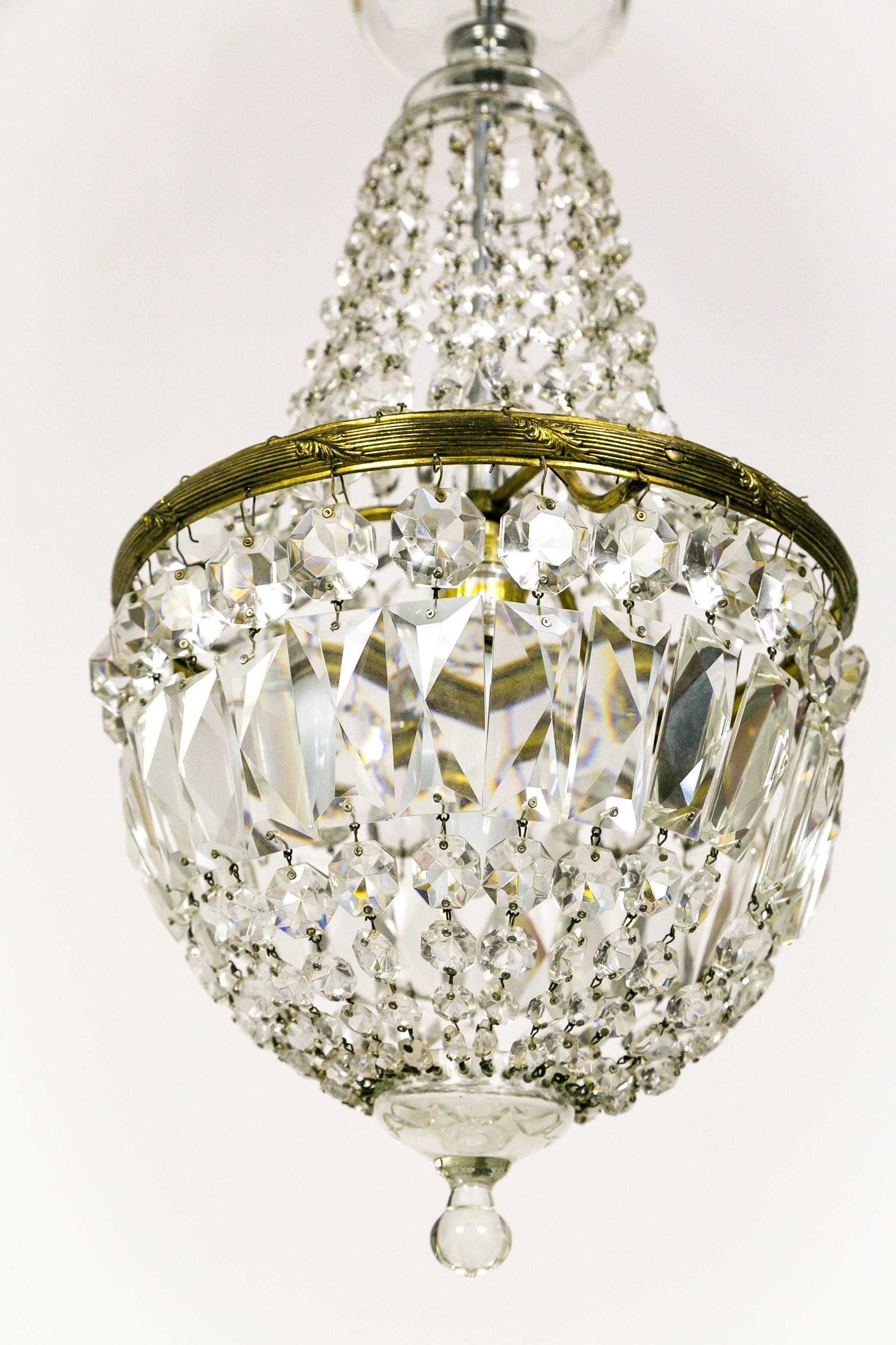 These Regency style chandeliers from the 1920s have radiant, closely placed crystal strands forming its basket shape. A stunning look with an intimate size. They have a glass crown bobesche and finial; and fine brass canopy and frame with delicate