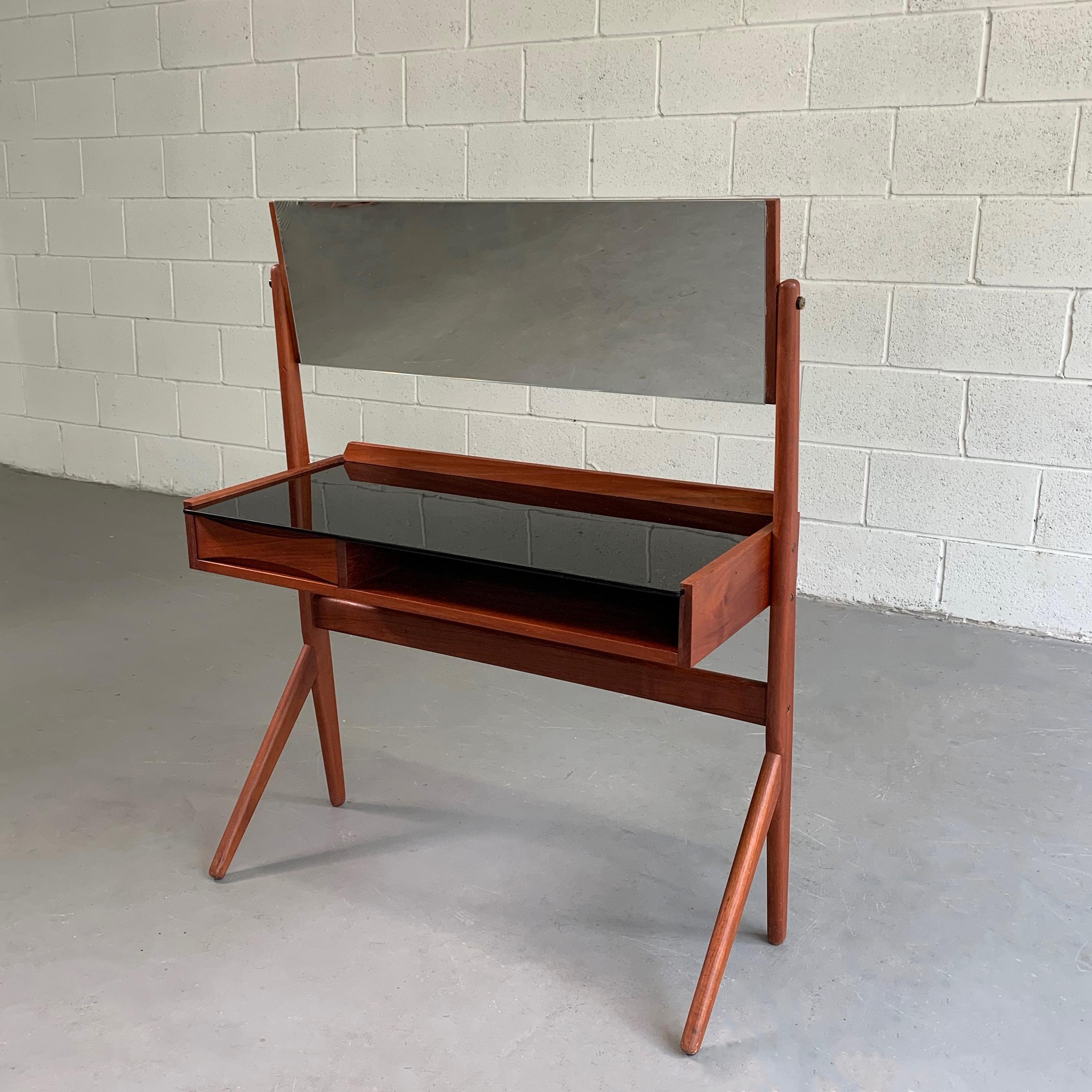Petite, Danish modern, teak vanity, dressing table by Arne Vodder for Ølholm Møebelfabrik features compass legs, black glass top and tilt adjustable mirror. Under the desk there is one drawer with bowtie pull and an open compartment. The table